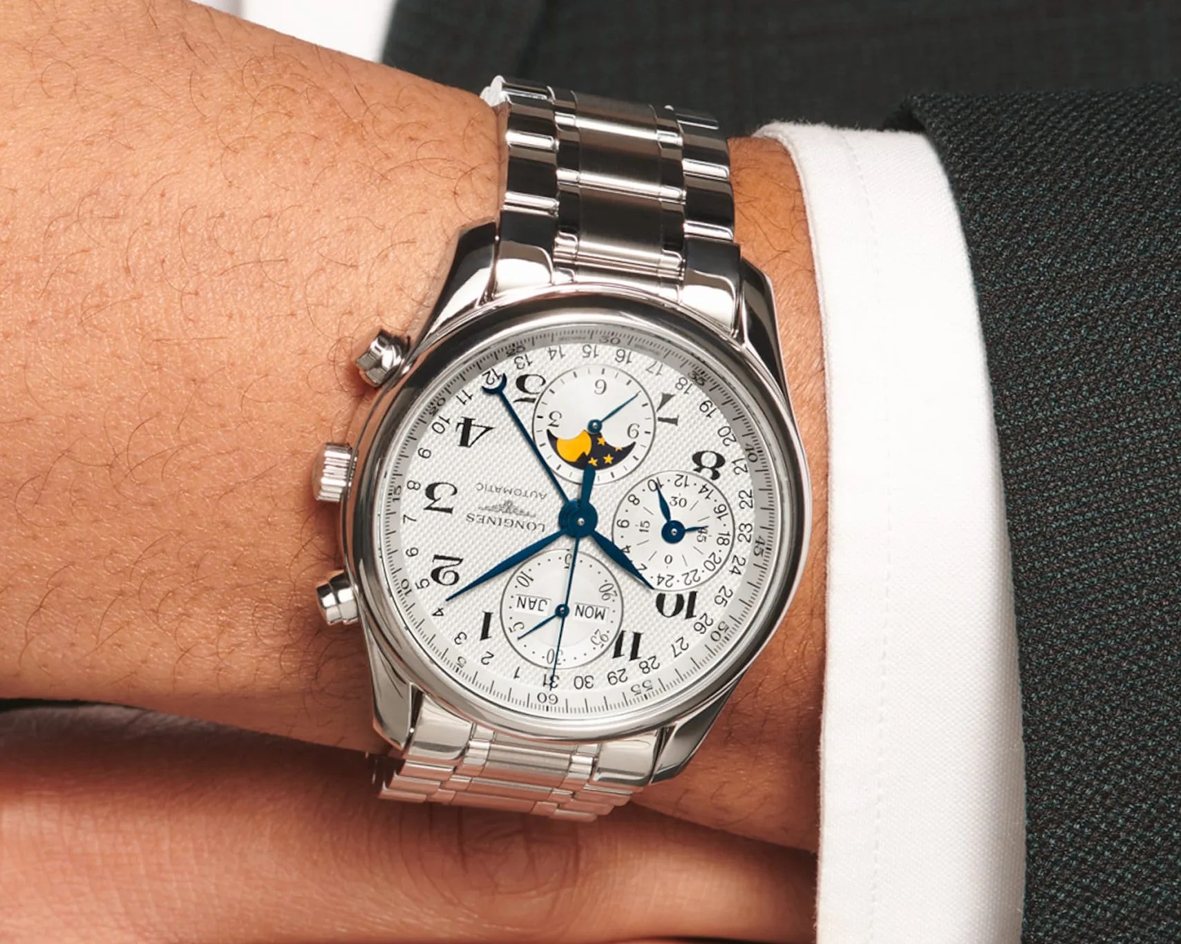 Silver Longines automatic wristwatch with white dial, blue hands, moon phase, and multiple subdials on a metal bracelet.
