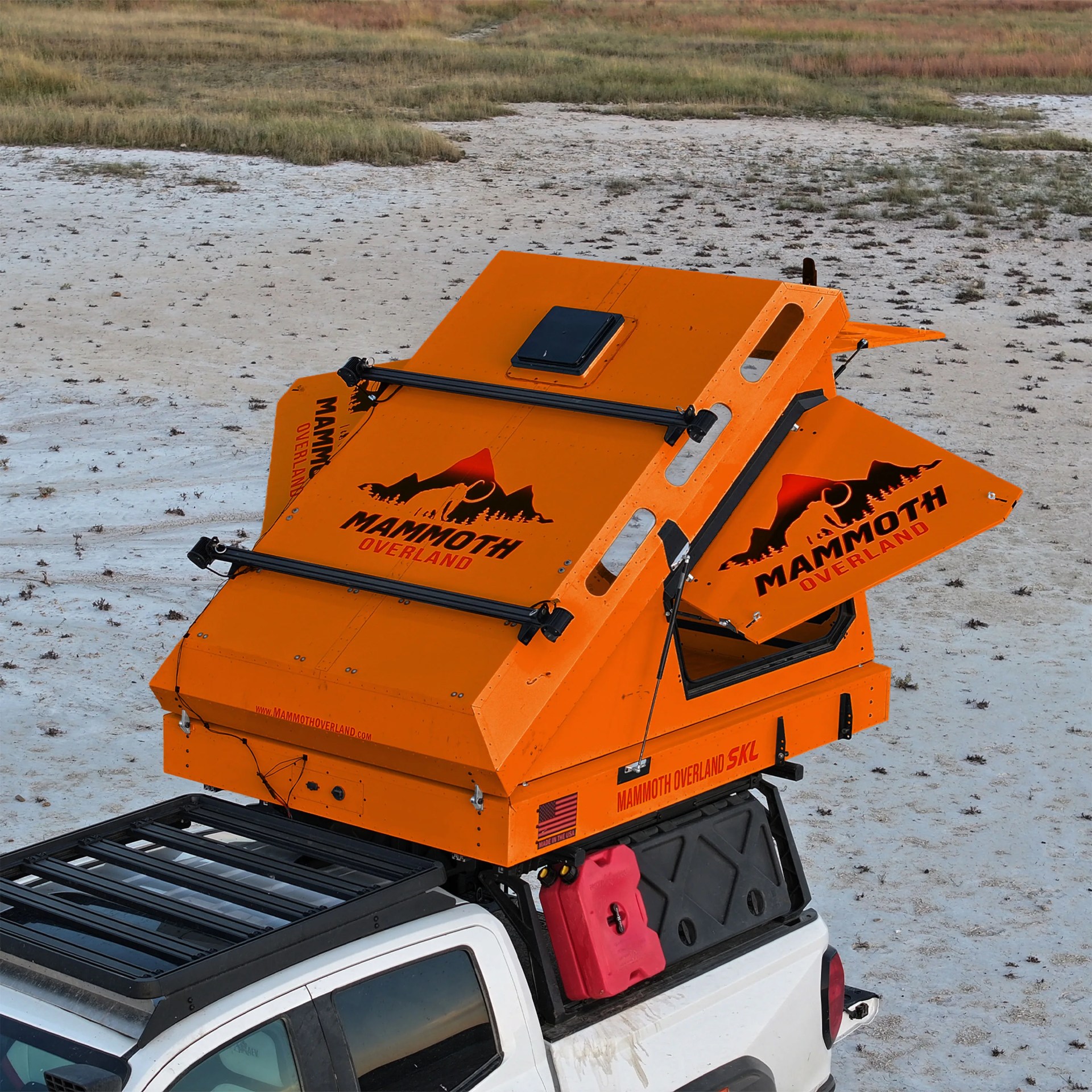 Orange Mammoth Overland rooftop camper mounted on a white pickup truck in a dry, grassy area.