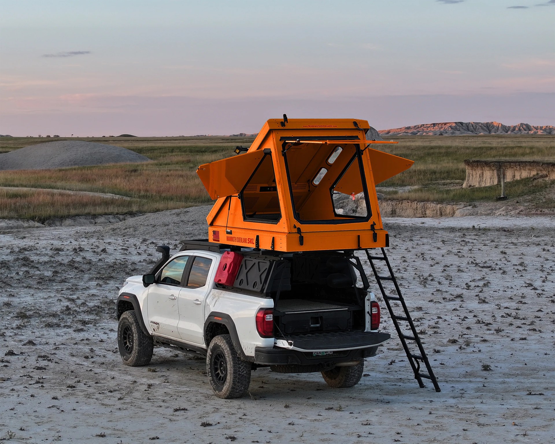 White pickup truck with black off-road tires and an orange rooftop tent with open windows and a ladder in a dry, grassy landscape.
