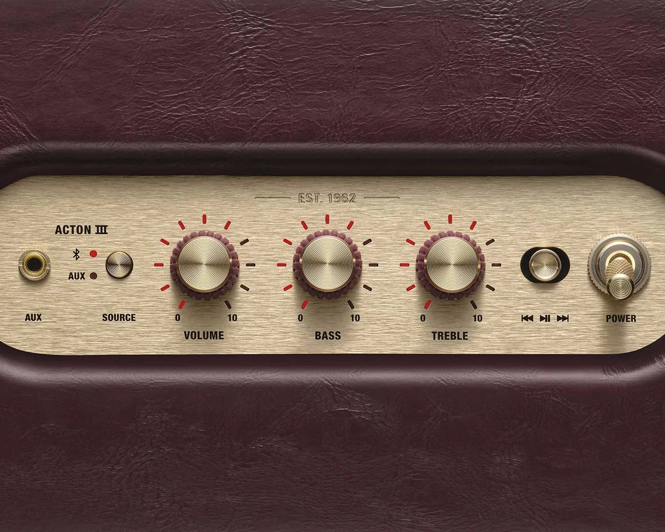 Close-up of a vintage-style audio control panel with volume, bass, treble knobs, source selector, and power switch on a brown leather background.