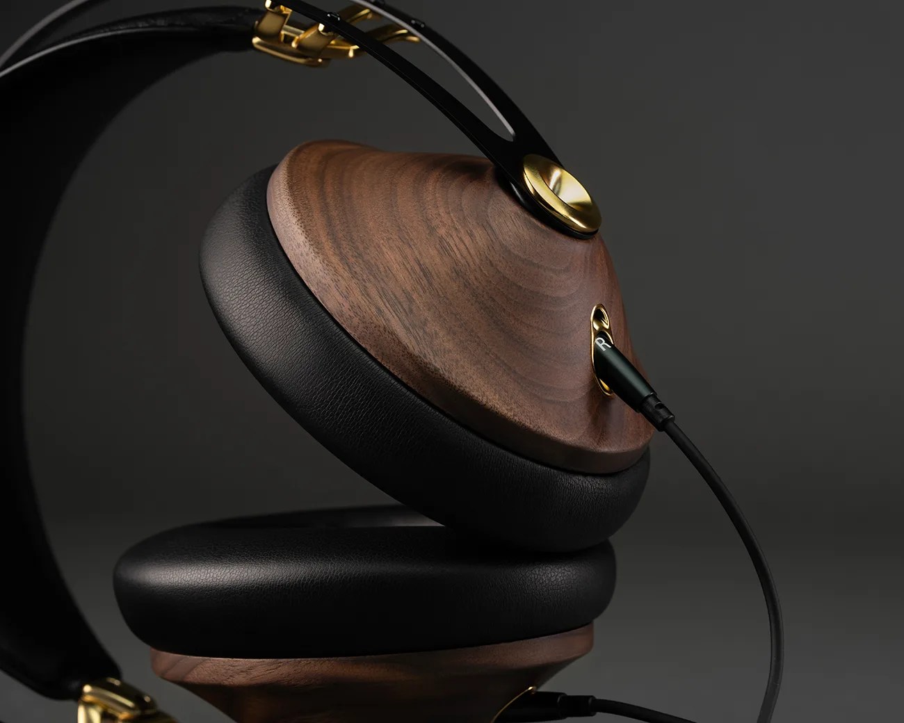 Over-ear headphones with wooden ear cups, black leather cushions, and gold metal accents with a cable plugged in.