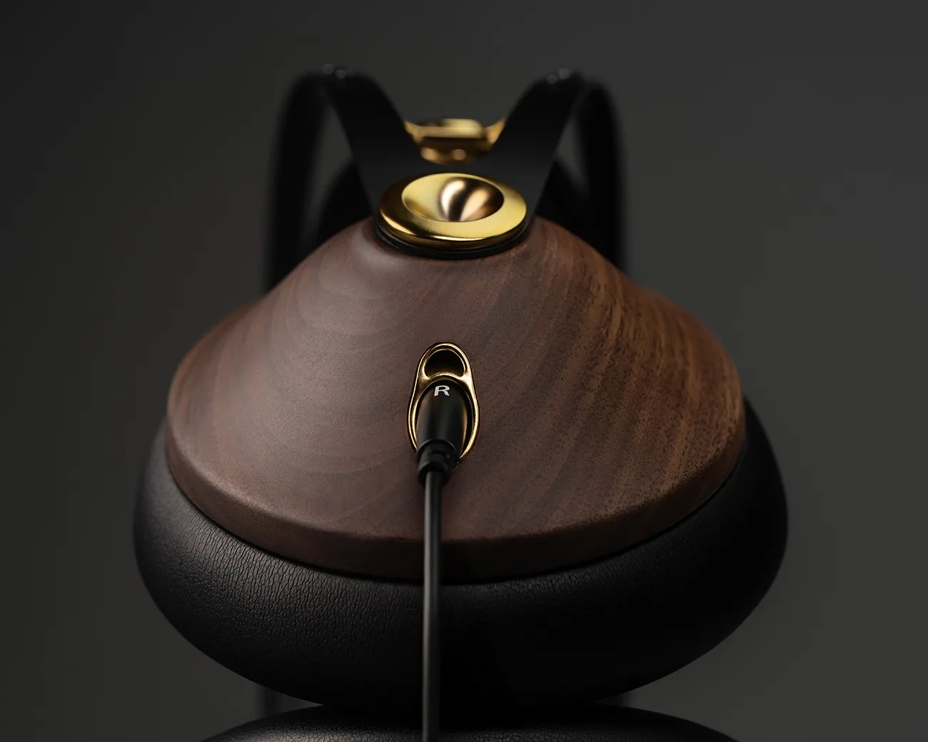 Over-ear headphone with dark wood ear cup, black leather padding, and gold metal accents with cable plugged in.