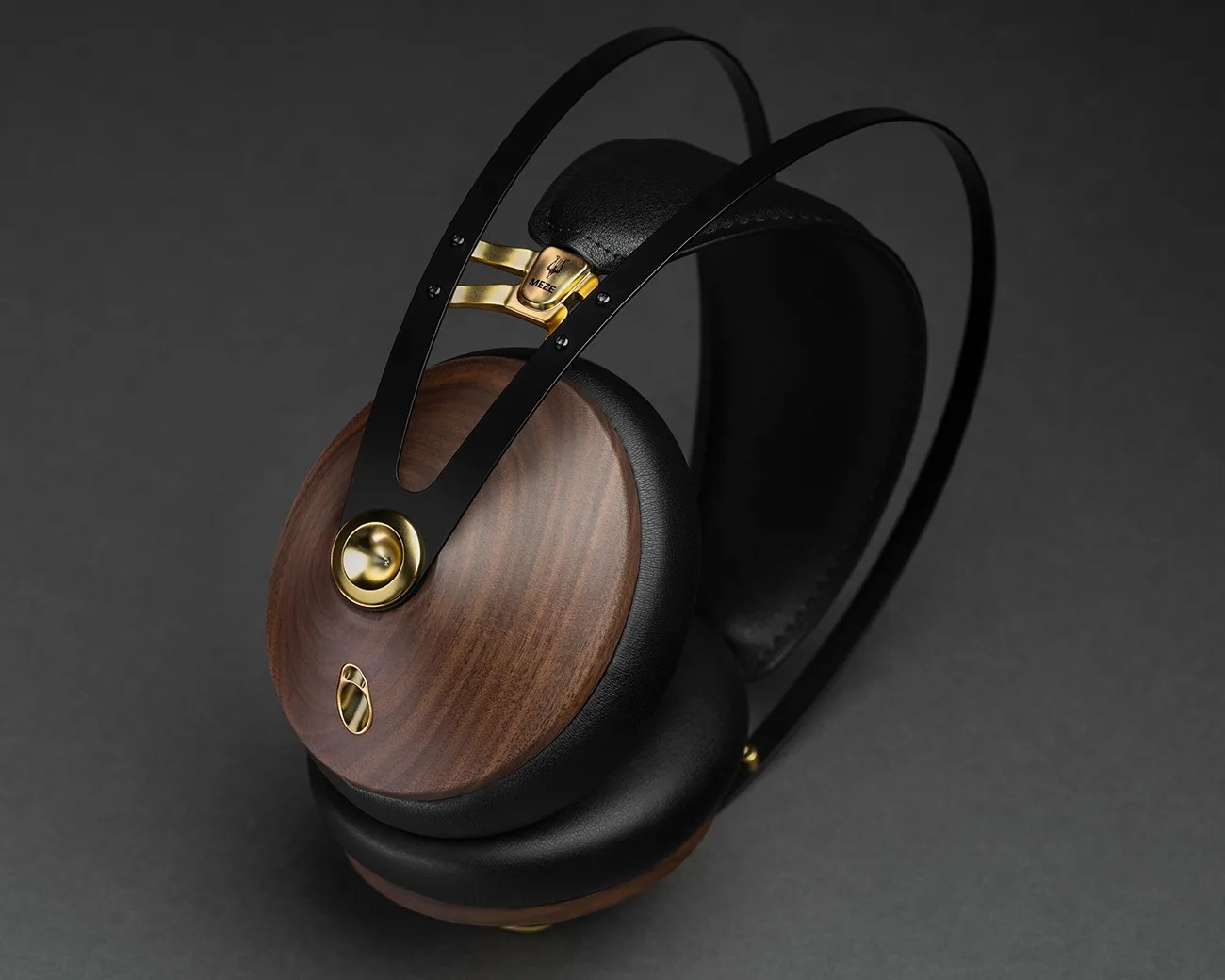 Over-ear headphones with wooden ear cups, black leather padding, and gold metal accents on a dark background.