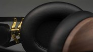 Close-up of black leather ear cushions and gold metal hinge on over-ear headphones with wooden ear cup.