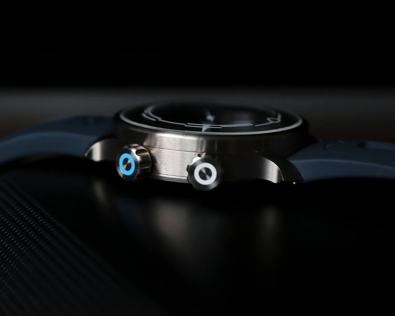 Close-up of a watch case with two crowns, one with a blue ring and the other with a white ring, attached to a blue strap.
