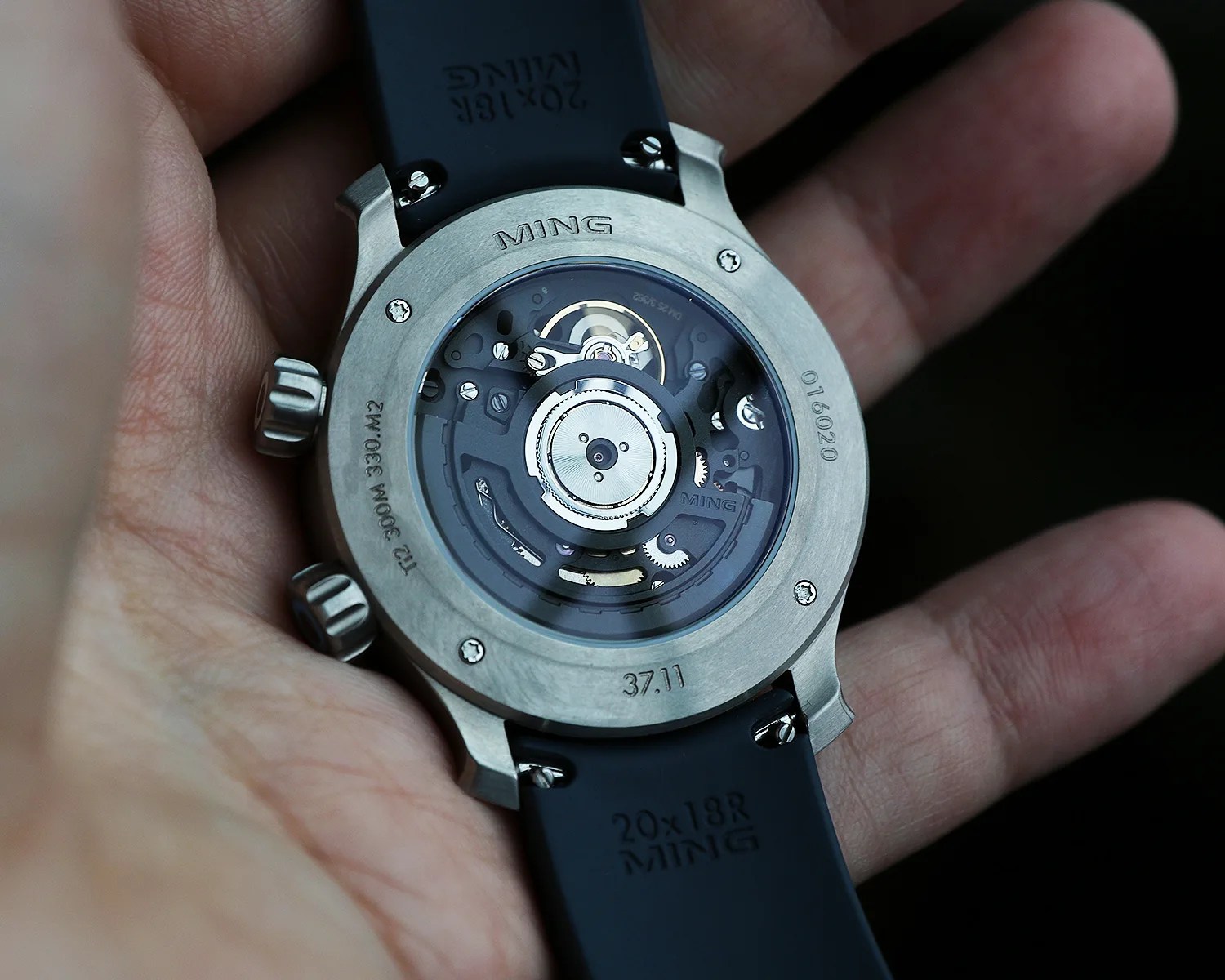 Close-up of the back of a Ming wristwatch showing the mechanical movement through a transparent case back with a black strap.