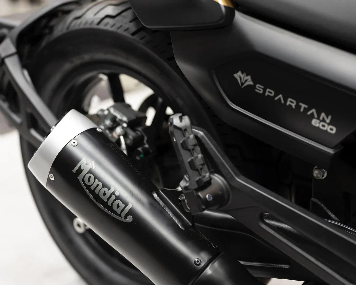 Close-up of black Mondial exhaust and footpeg on a black Spartan 600 motorcycle rear wheel.
