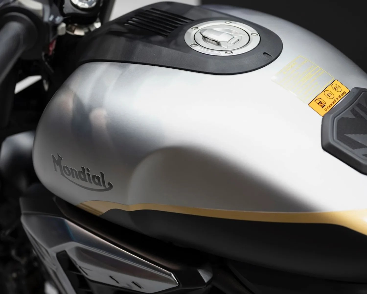 Silver motorcycle fuel tank with black and gold accents and "Mondial" logo on the side.