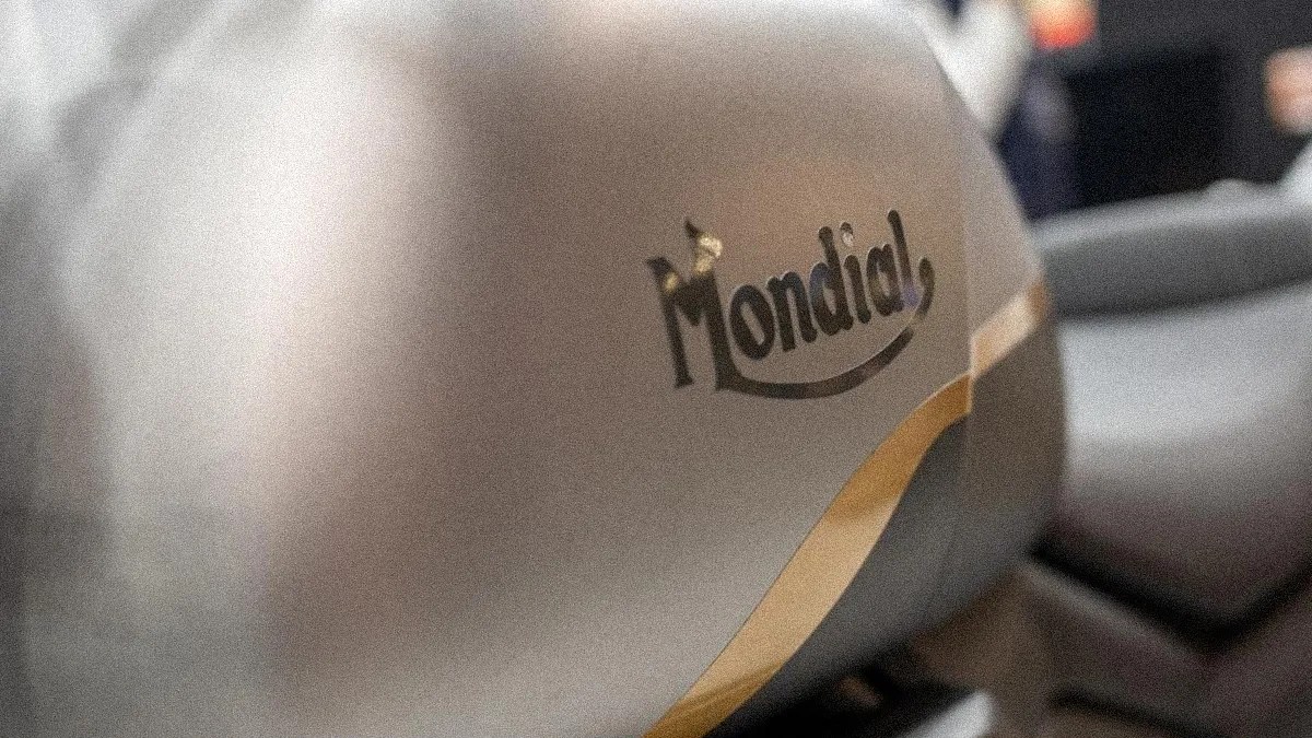 Close-up of a beige motorcycle fuel tank with the black "Mondial" logo and a yellow stripe.