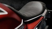 Close-up of a black leather motorcycle seat with white stitching on a red and black bike.