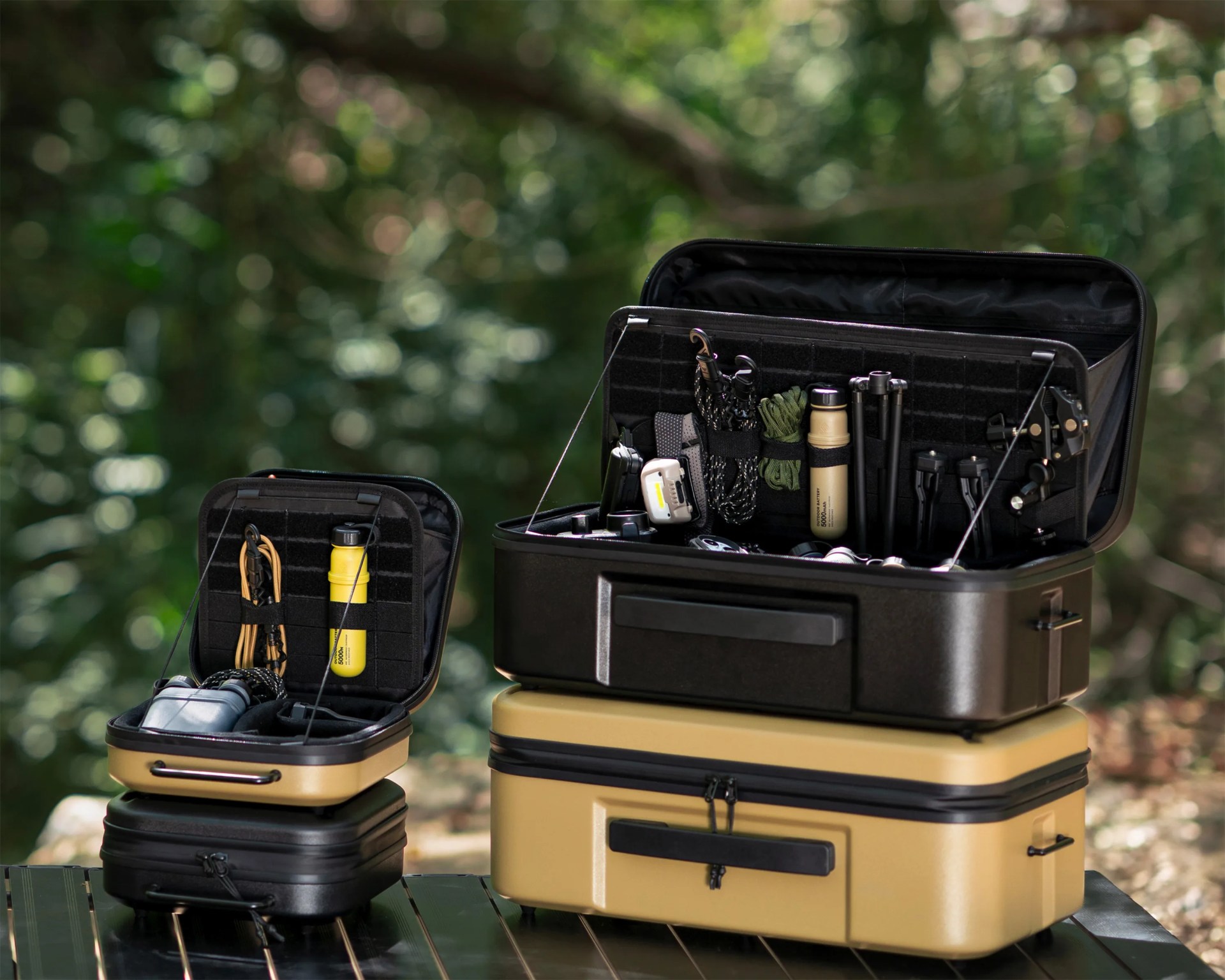 Two open hard-shell cases with organized compartments holding outdoor gear, set on a table with a blurred forest background.