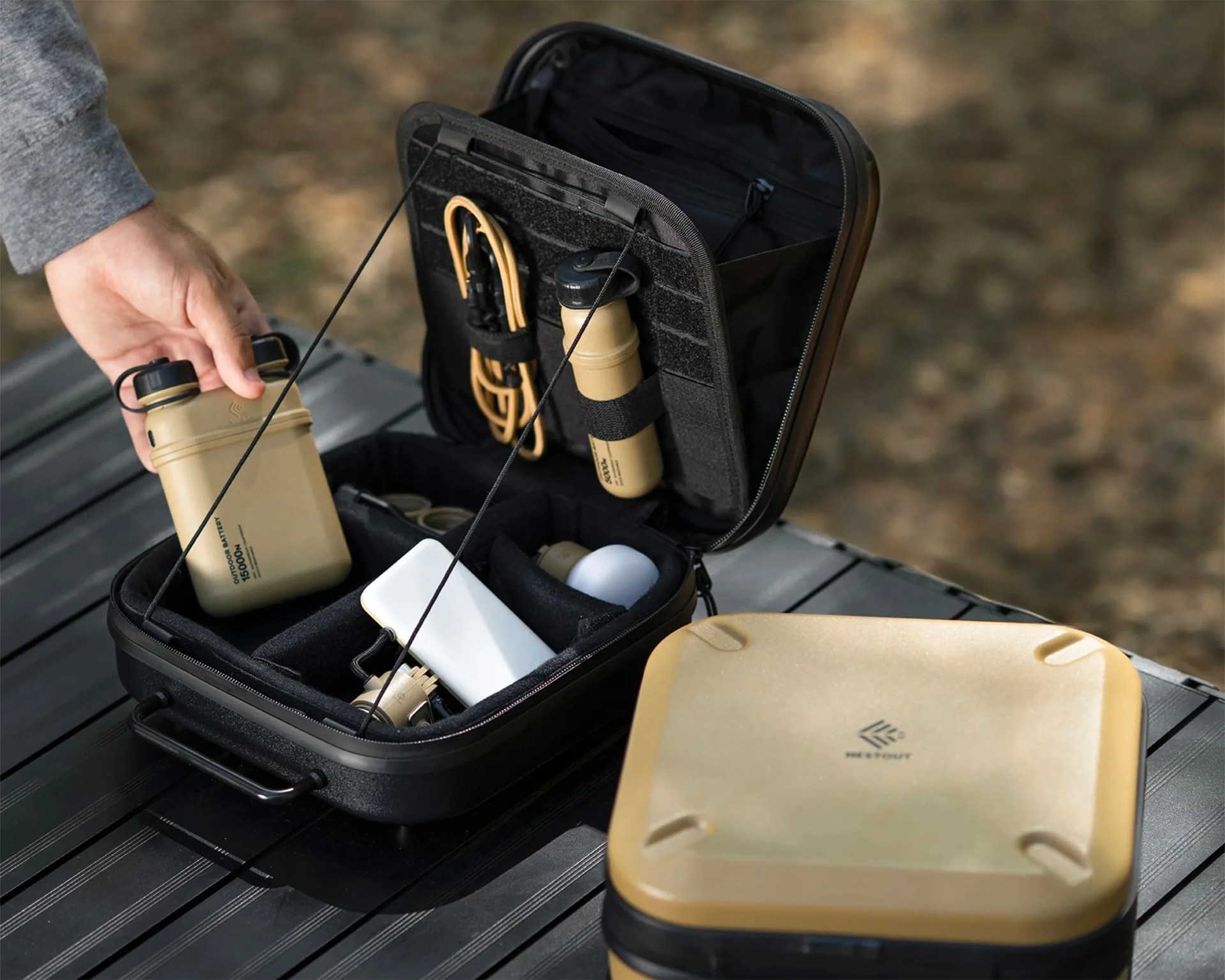 Black and tan hard-shell organizer case open on a table with tan outdoor battery and cables inside.
