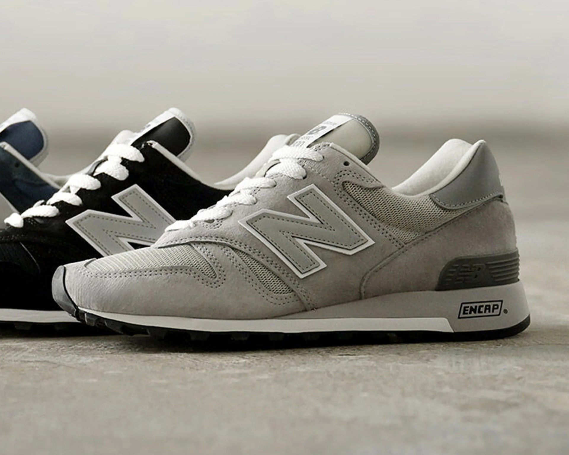 Pair of New Balance sneakers, one gray and one black, with white laces and ENCAP midsoles on a concrete floor.