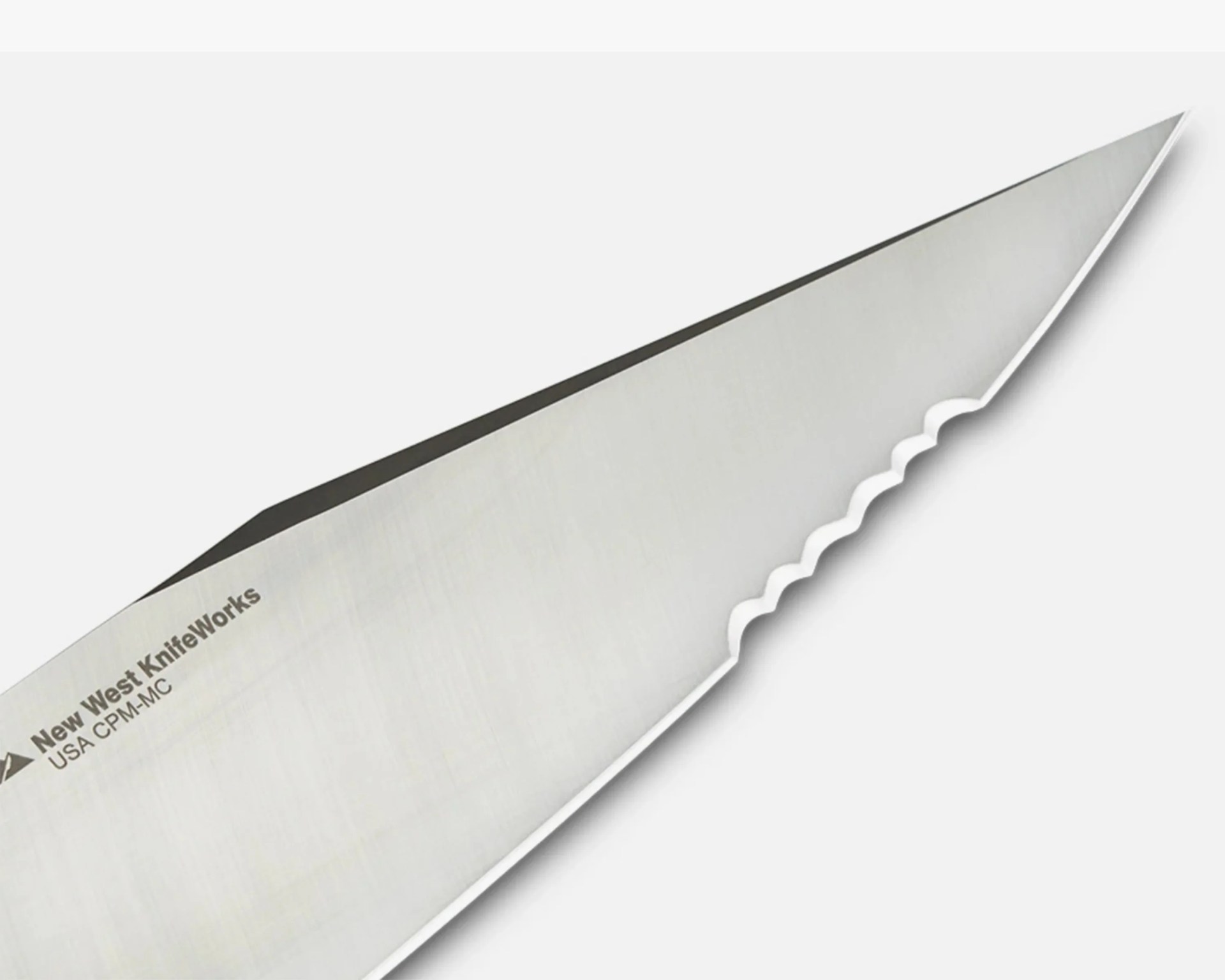 Close-up of a stainless steel serrated knife blade with "New West KnifeWorks USA CPM-MC" text.