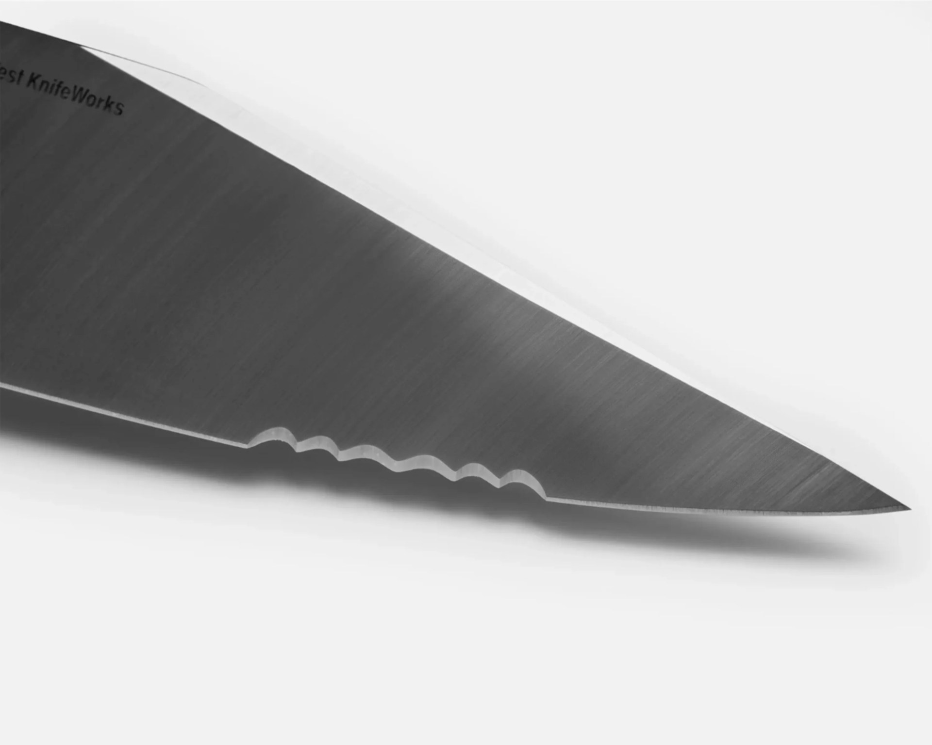 Close-up of a serrated stainless steel knife blade with a brushed finish on a white background.