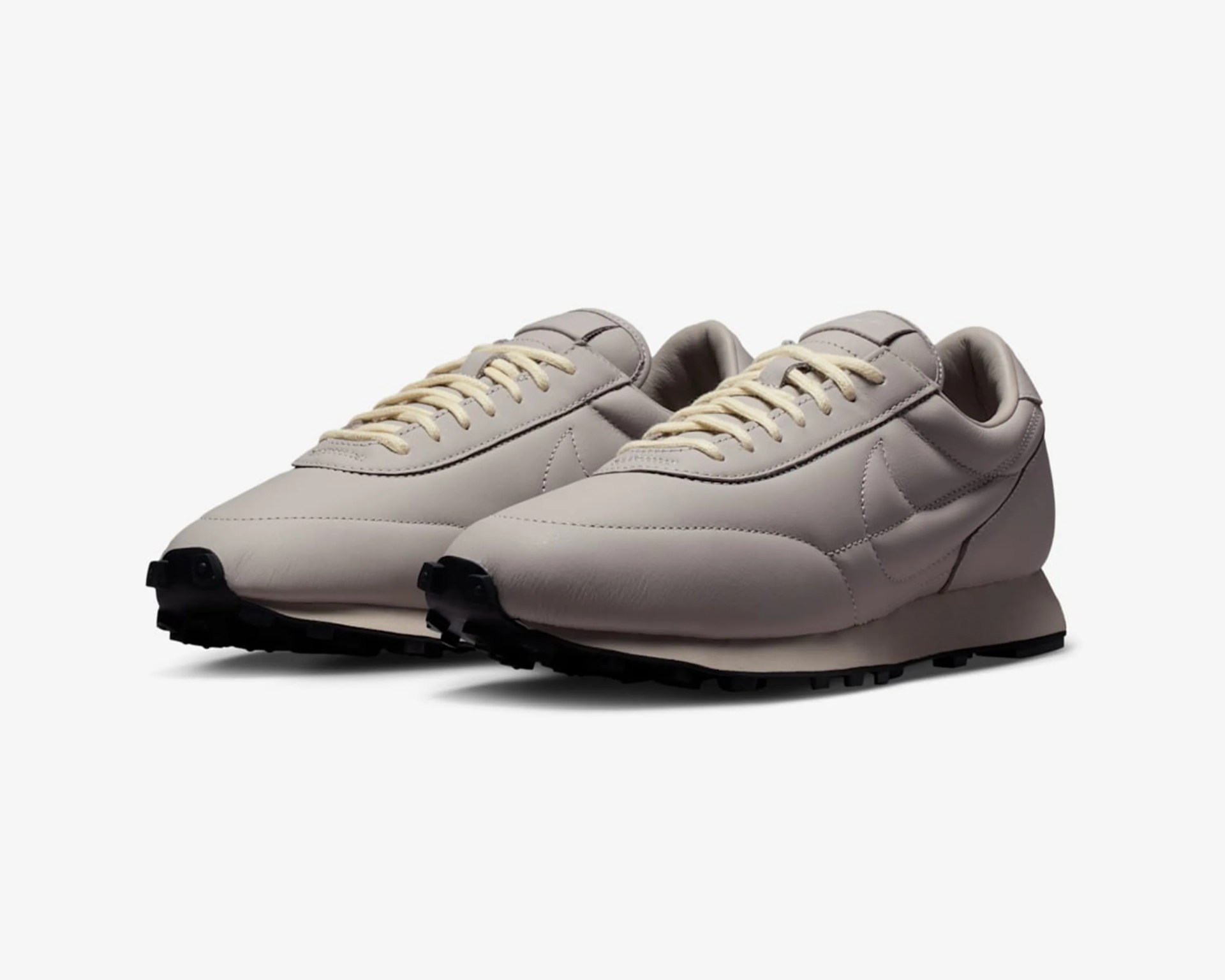 Pair of light beige leather Nike sneakers with cream laces and black rubber soles.