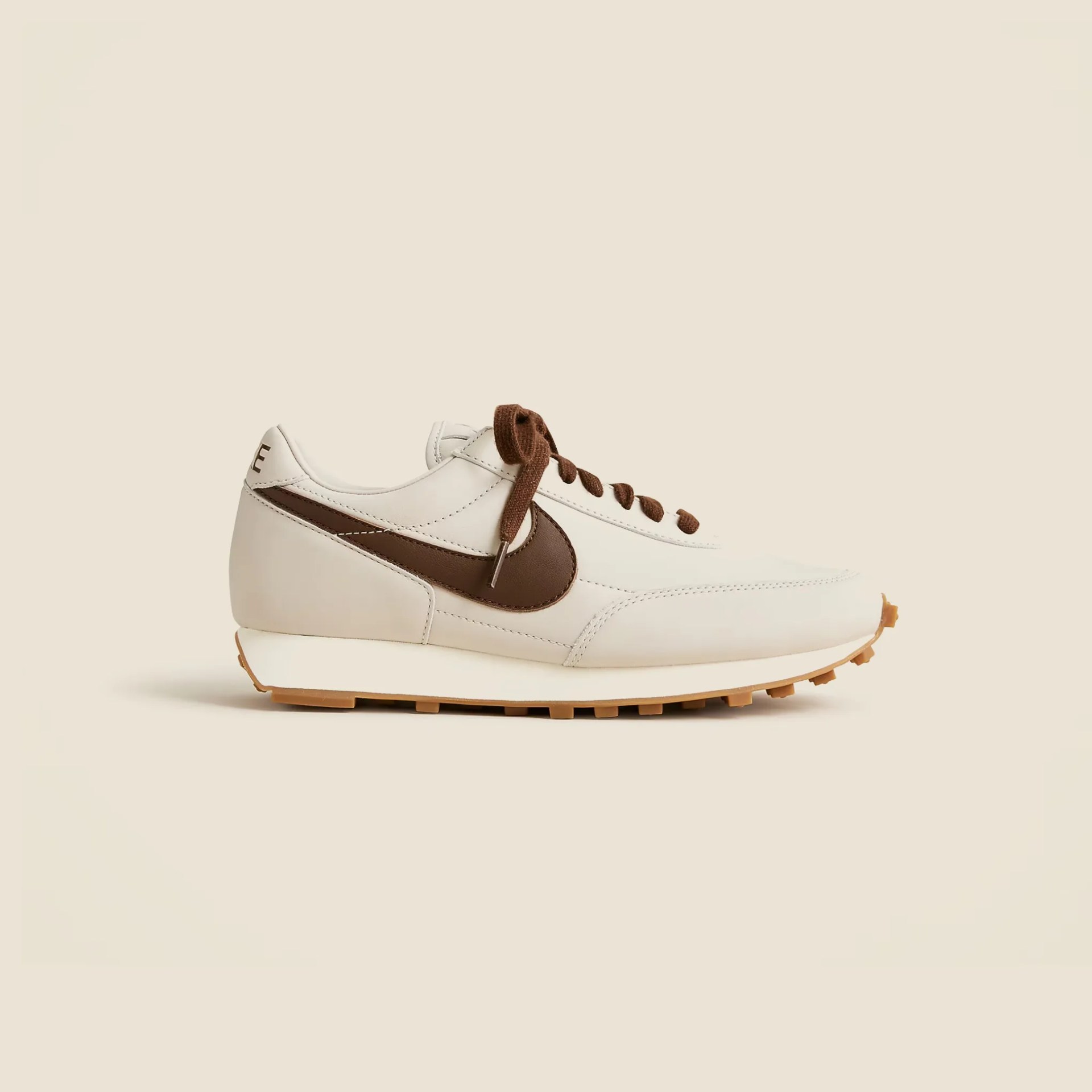 Off-white leather sneaker with brown Nike swoosh and laces, and a gum rubber sole.