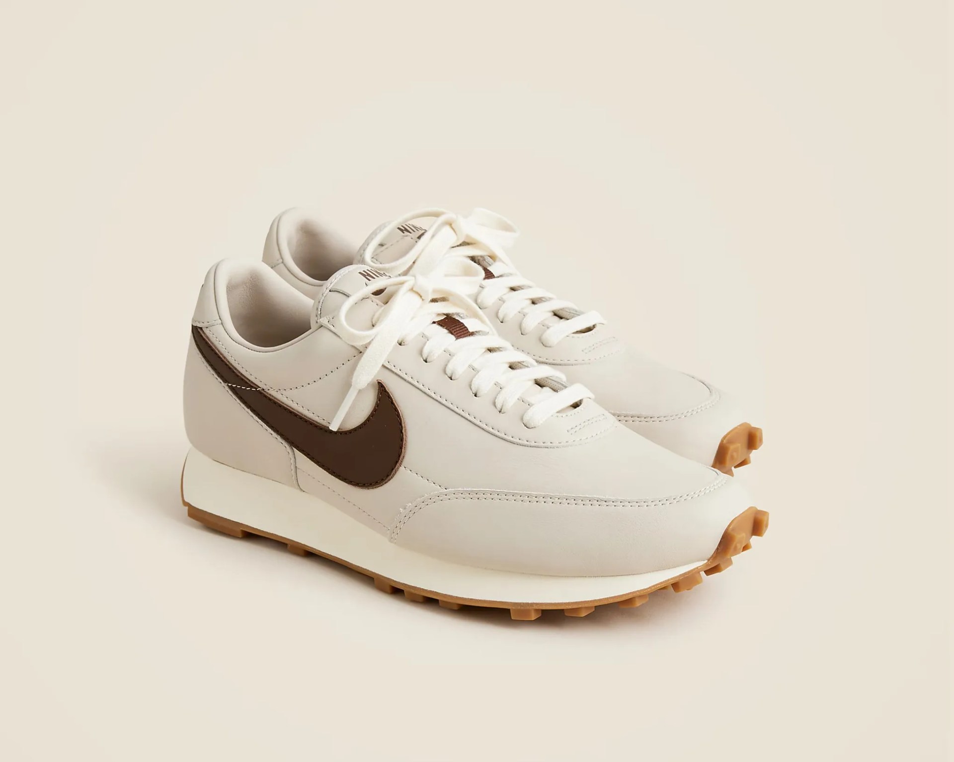 Pair of off-white Nike sneakers with brown swoosh logos and gum rubber soles on a beige background.
