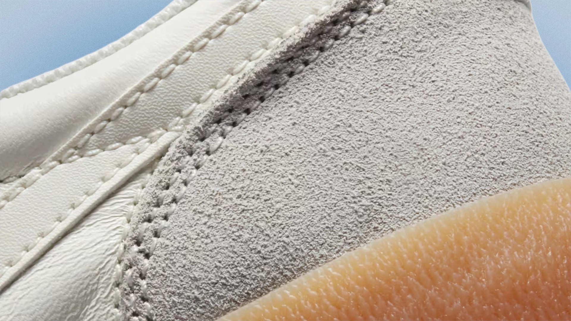 Close-up of white leather and gray suede shoe upper with detailed stitching and a light brown rubber sole.