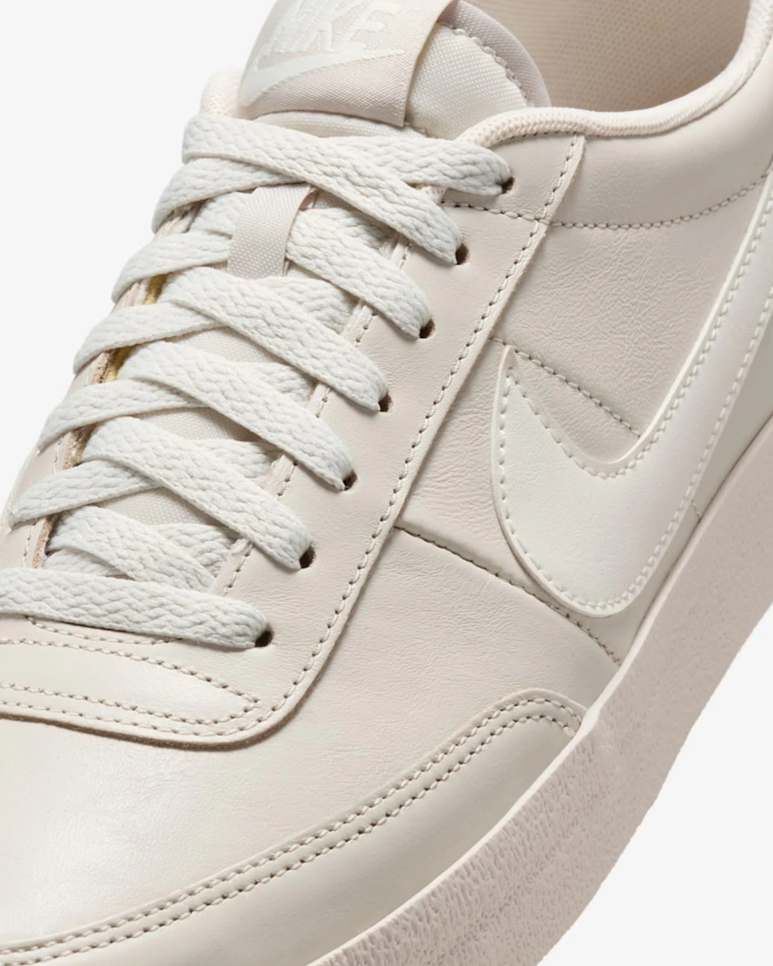 Close-up of a cream-colored Nike sneaker with textured laces and a stitched swoosh logo.
