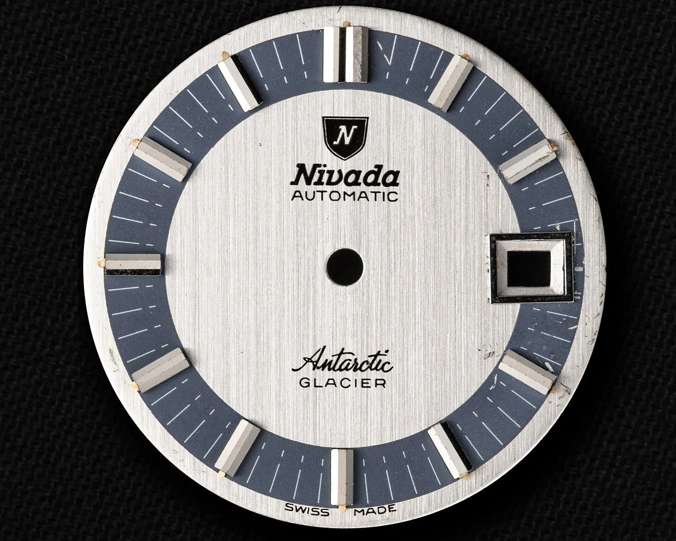Round silver and blue Nivada Antarctic Glacier watch dial with rectangular hour markers and a date window at 3 o'clock.