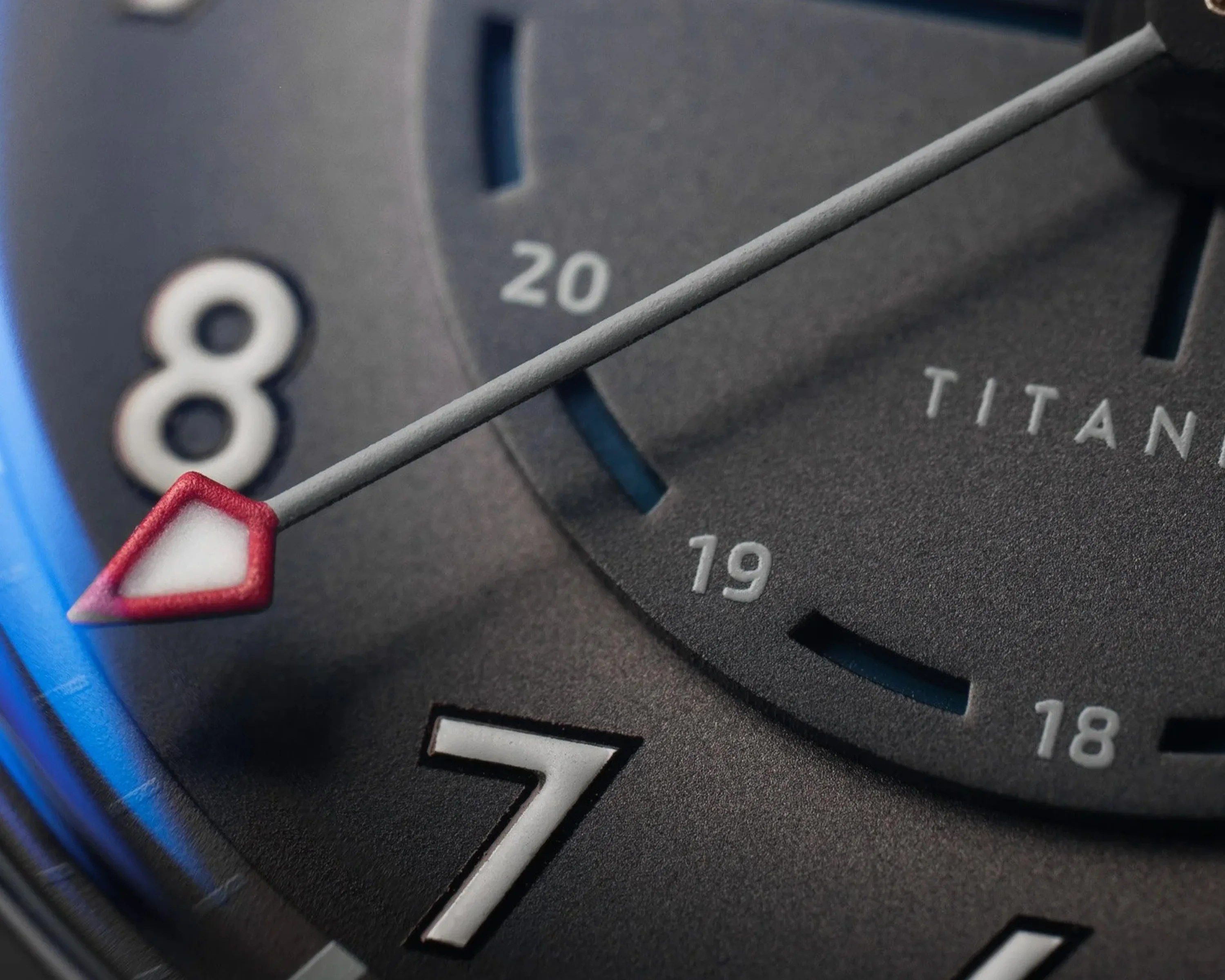 Close-up of a black watch face showing white numbers 7 and 8, a red-tipped hand, and the word "TITAN" partially visible.