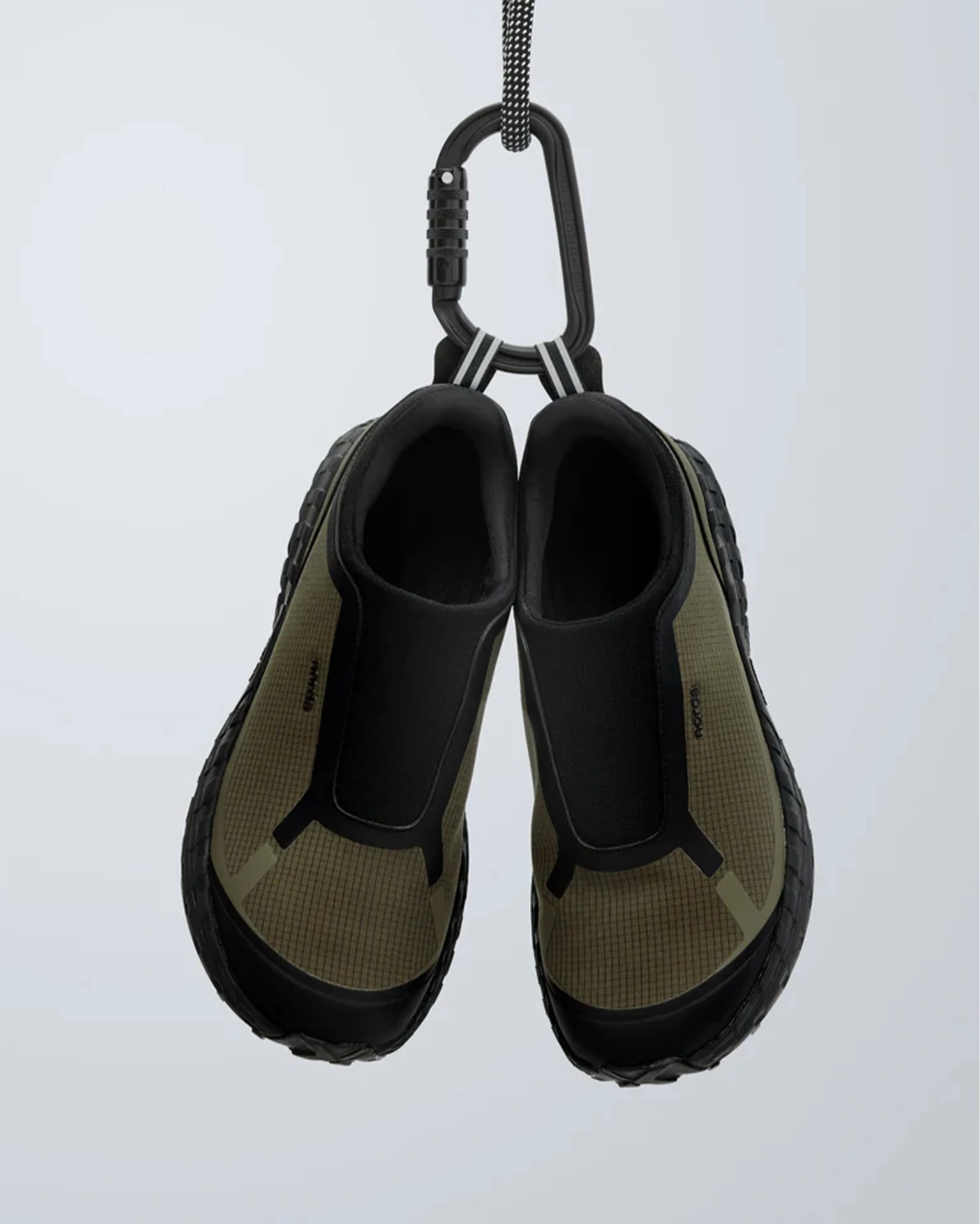 Pair of olive green and black slip-on shoes hanging from a black carabiner clip.