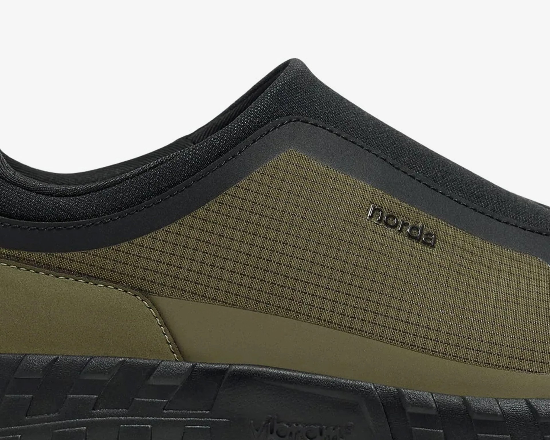 Close-up of an olive green and black shoe with textured fabric and "norda" logo on the side above a black sole.