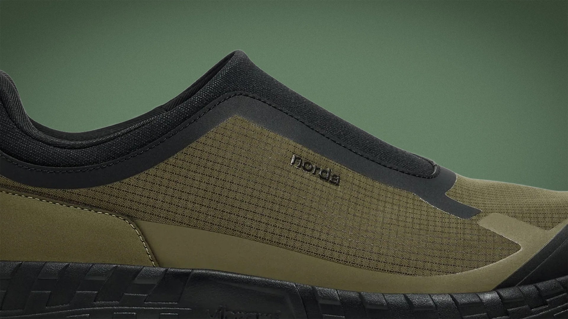 Close-up of an olive green and black Norda shoe with textured fabric and a thick black sole.