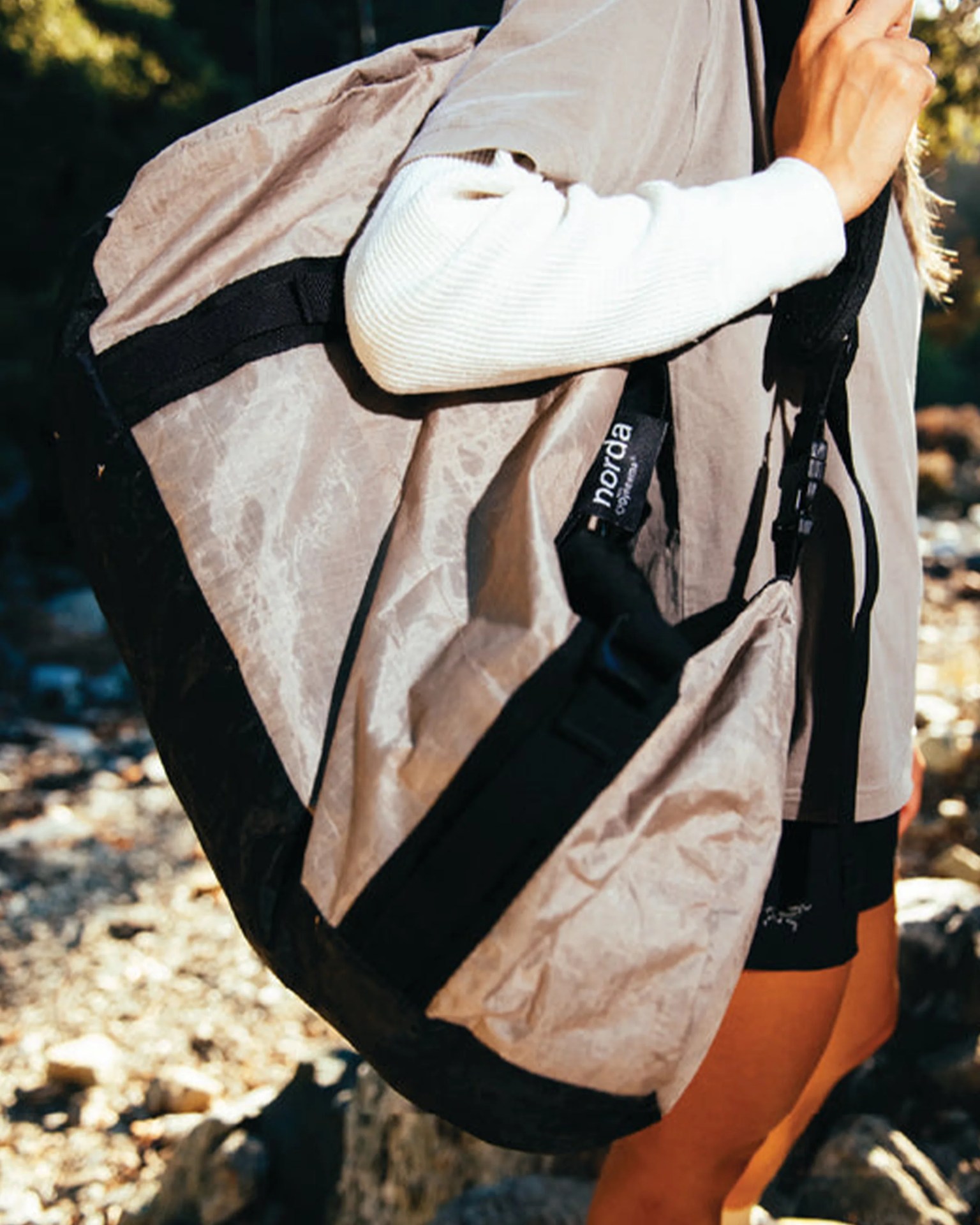 Light brown and black large shoulder bag with "norda" tag worn by a person outdoors.