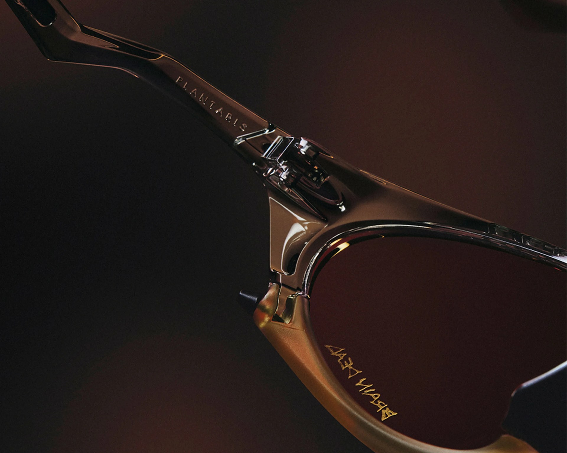 Close-up of a glossy black eyeglass frame hinge with "PLANTARIS" engraved on the arm and gold text on the lens.