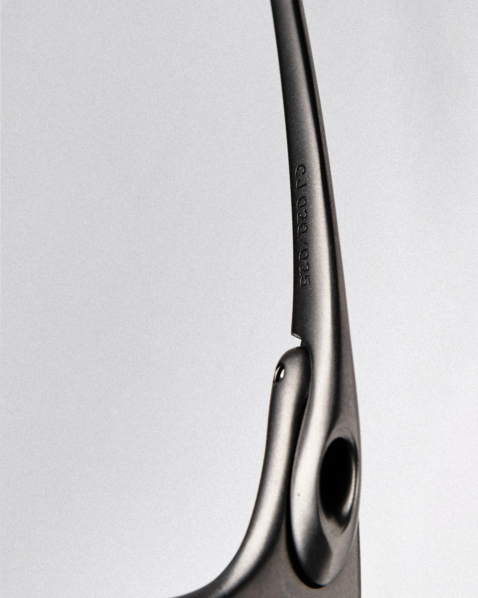 Close-up of a matte black eyeglass temple arm with engraved numbers "CJ 020/025" on a light gray background.