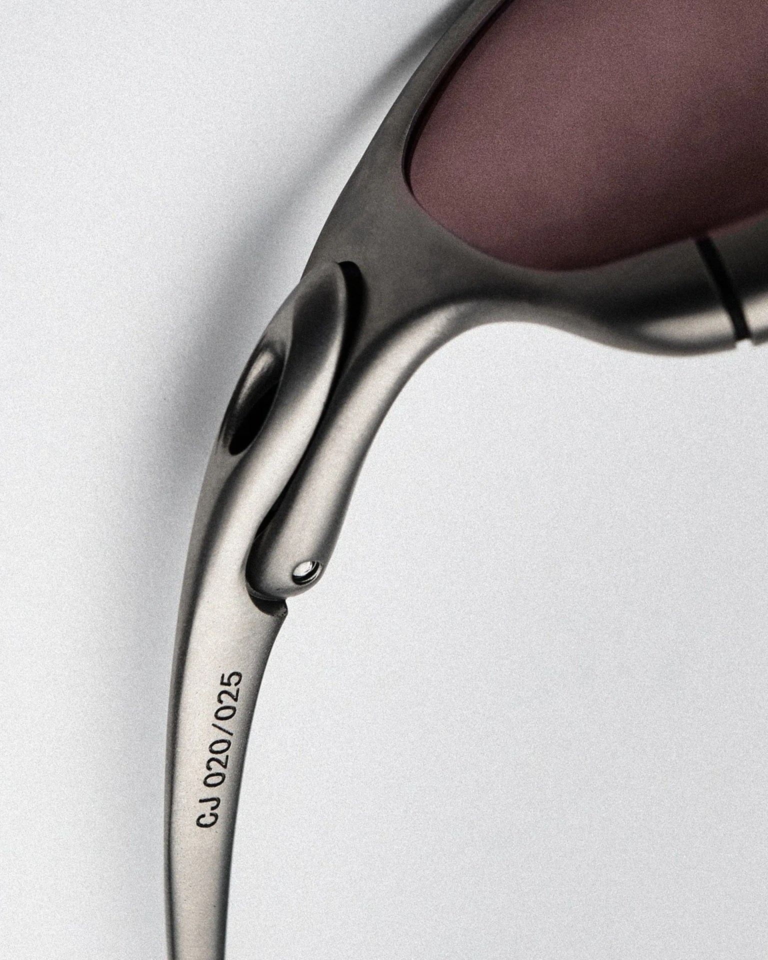 Close-up of a matte silver eyeglass arm with the code "CJ 020/025" printed on it and a purple lens frame.