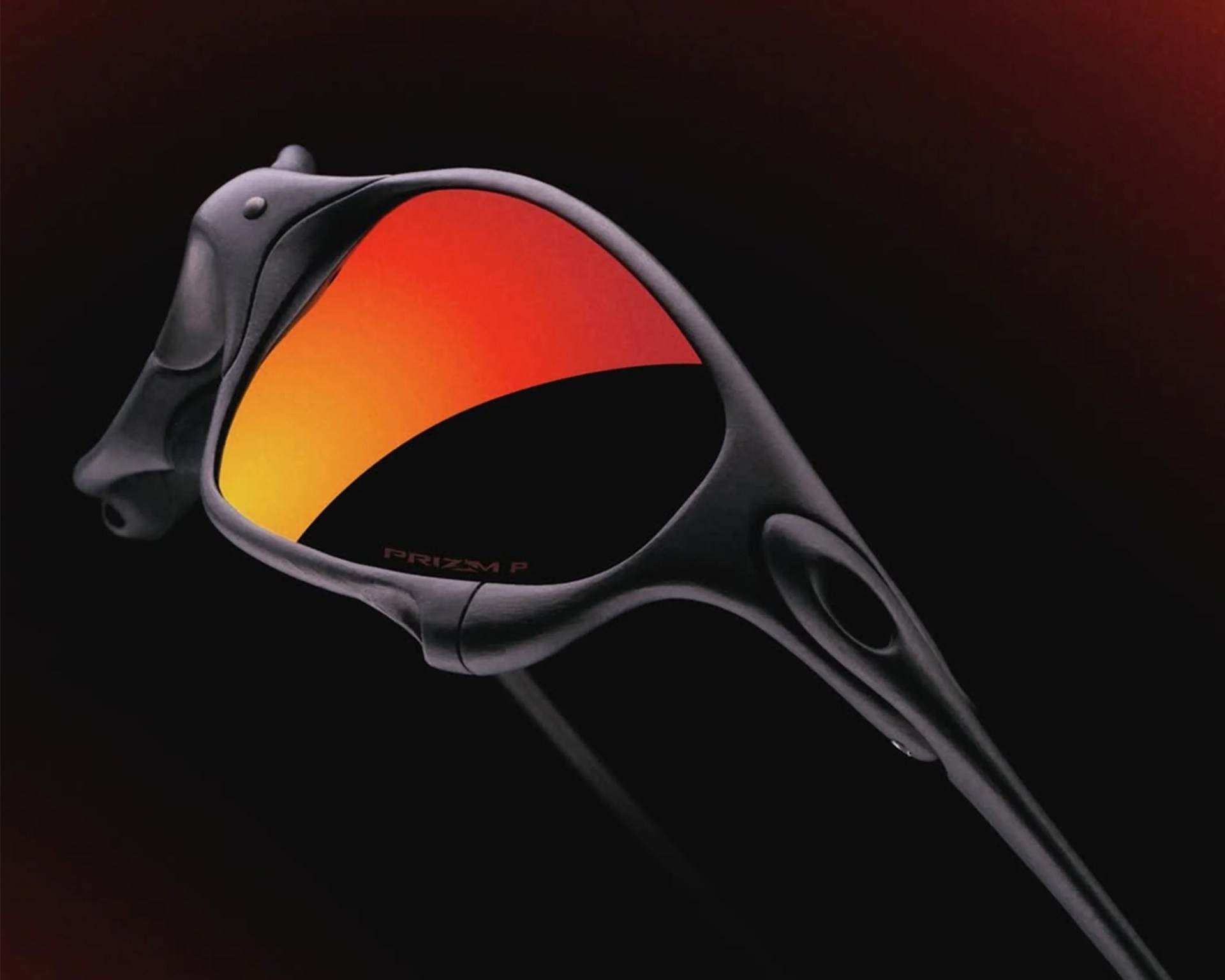 Black matte Oakley sunglasses with orange-red reflective Prizm lenses against a dark background.