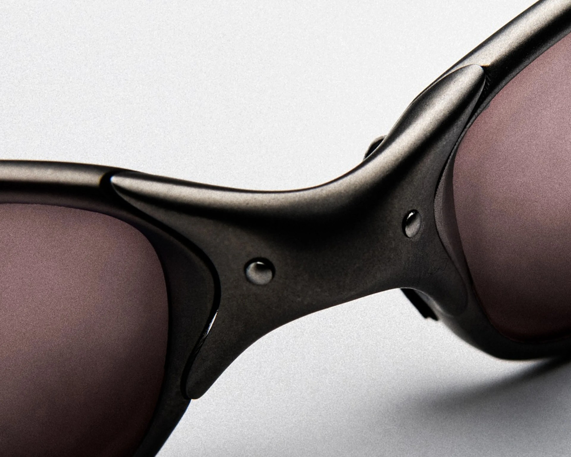 Close-up of black matte sunglasses frame with purple-tinted lenses on a light background.