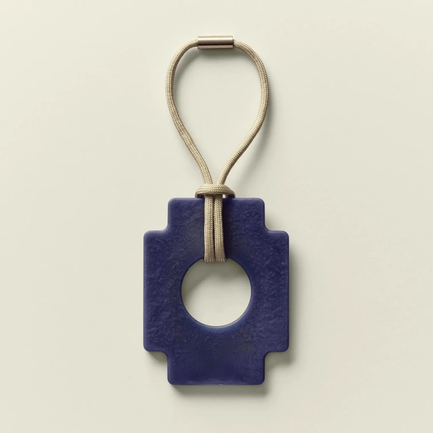 Blue geometric pendant with a central circular cutout attached to a beige cord loop.