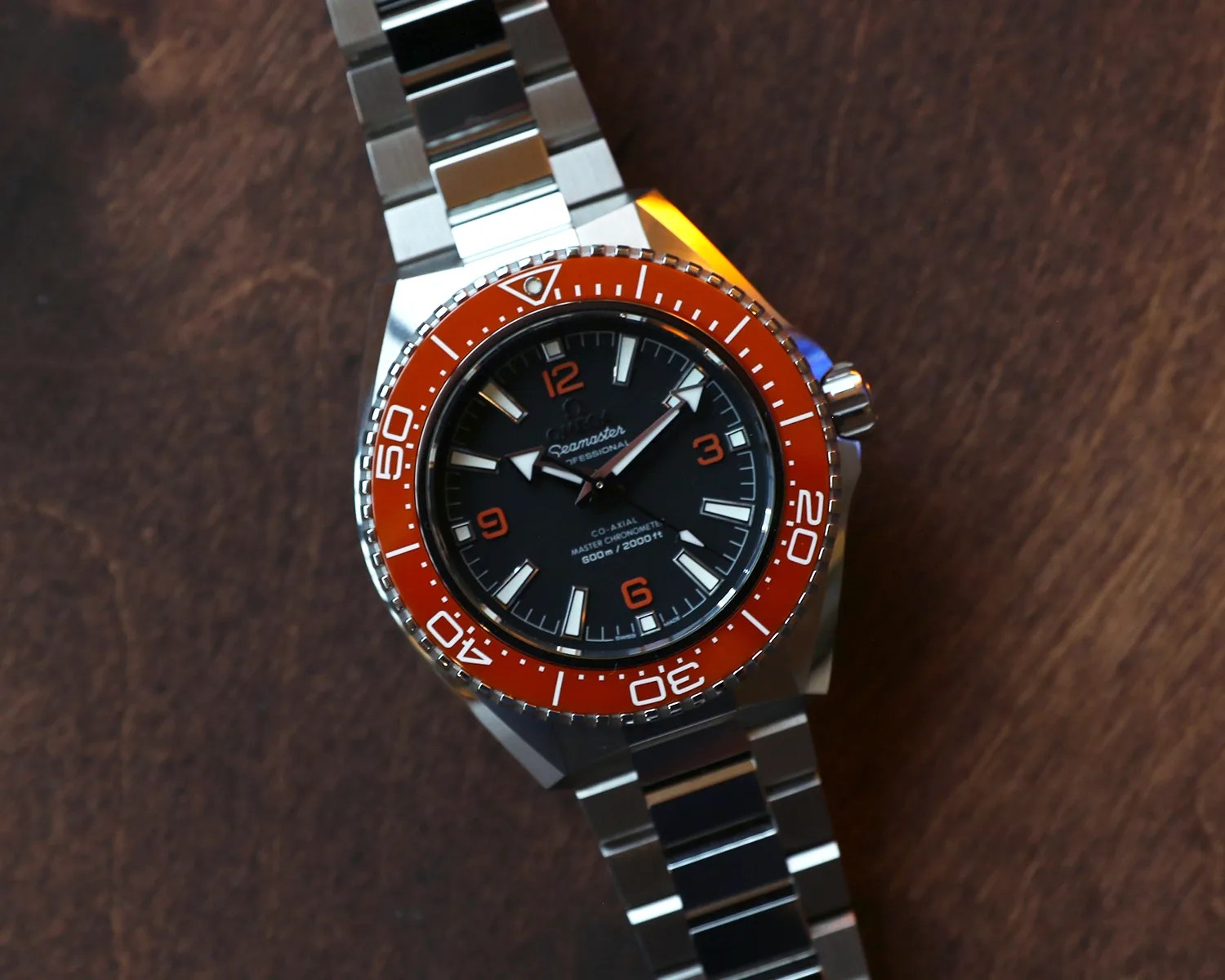 Stainless steel Omega Seamaster watch with black dial and orange bezel on a wooden surface.