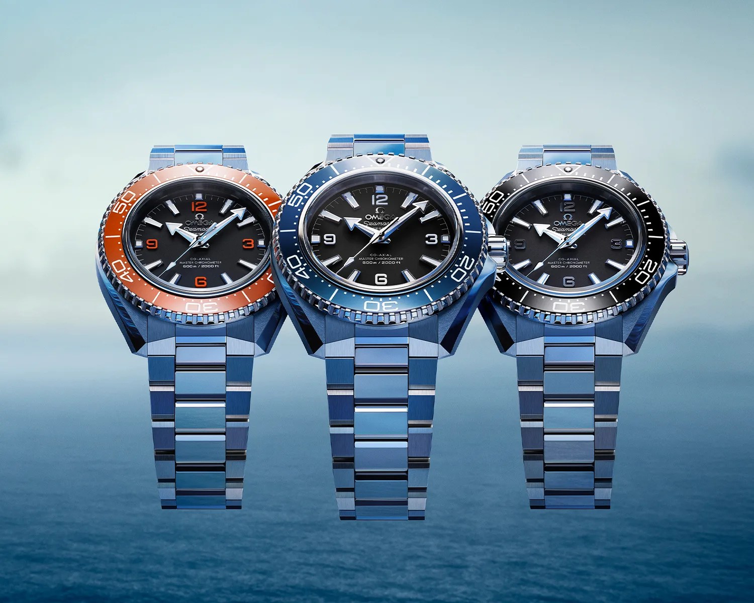 Three Omega Seamaster dive watches with stainless steel bracelets and black dials, featuring orange, blue, and black bezels.