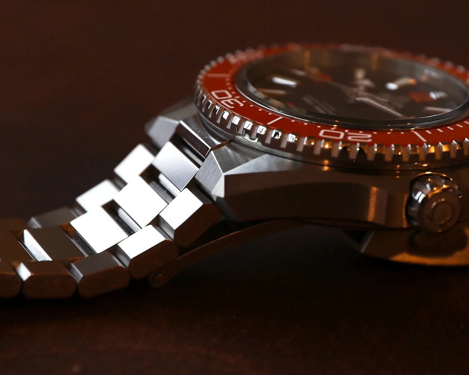 Close-up of a stainless steel watch with an orange bezel and metal link bracelet on a dark surface.