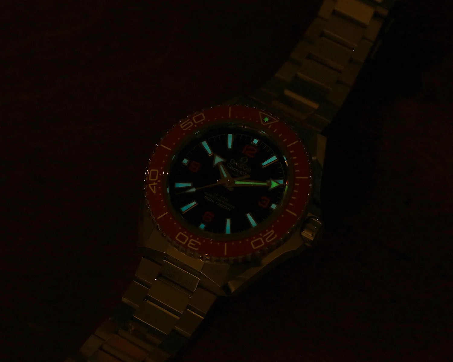 Omega Seamaster wristwatch with glowing blue hour markers and hands, orange bezel, and metal bracelet.