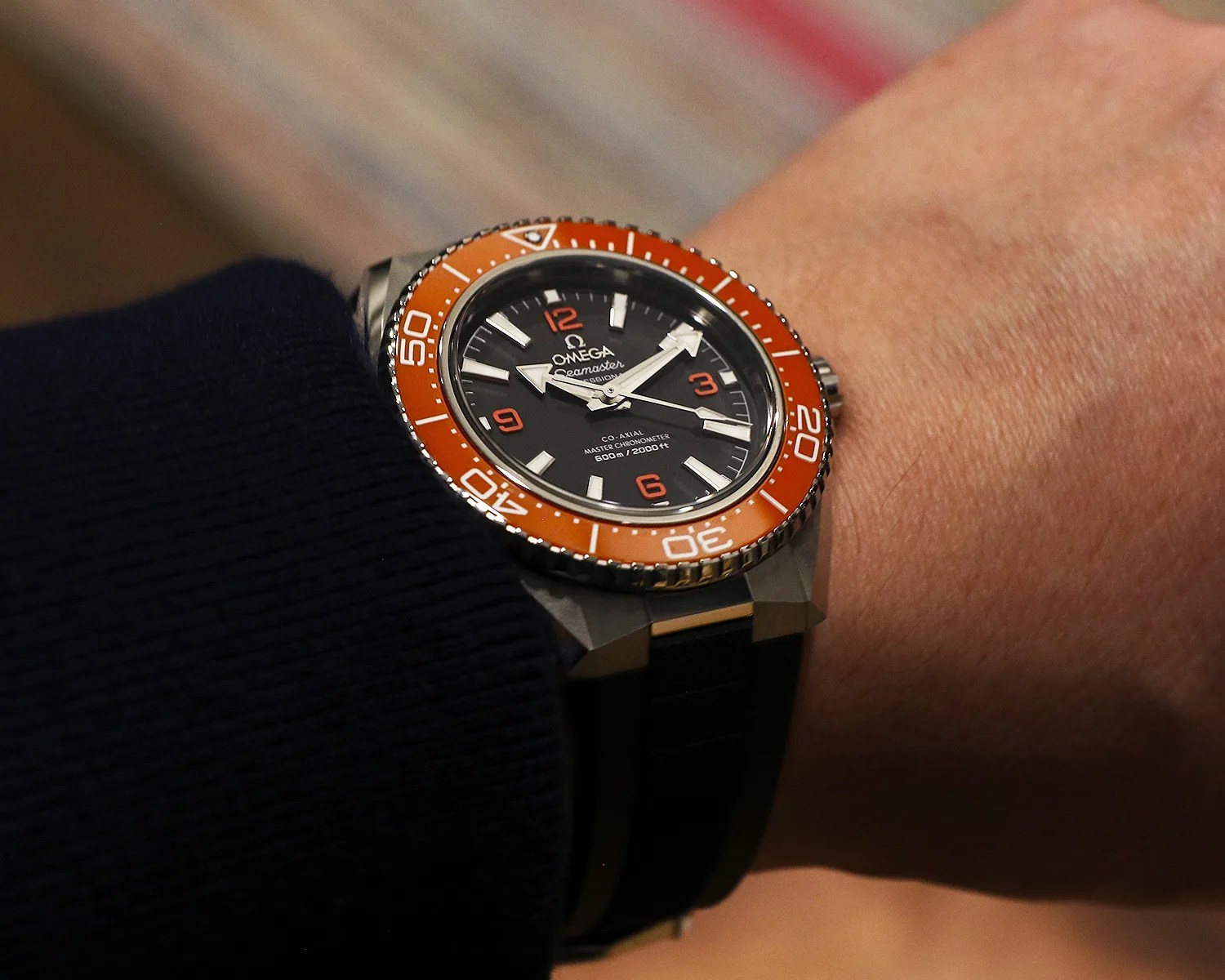 Omega Seamaster wristwatch with black dial, orange bezel, and black strap worn on a wrist.