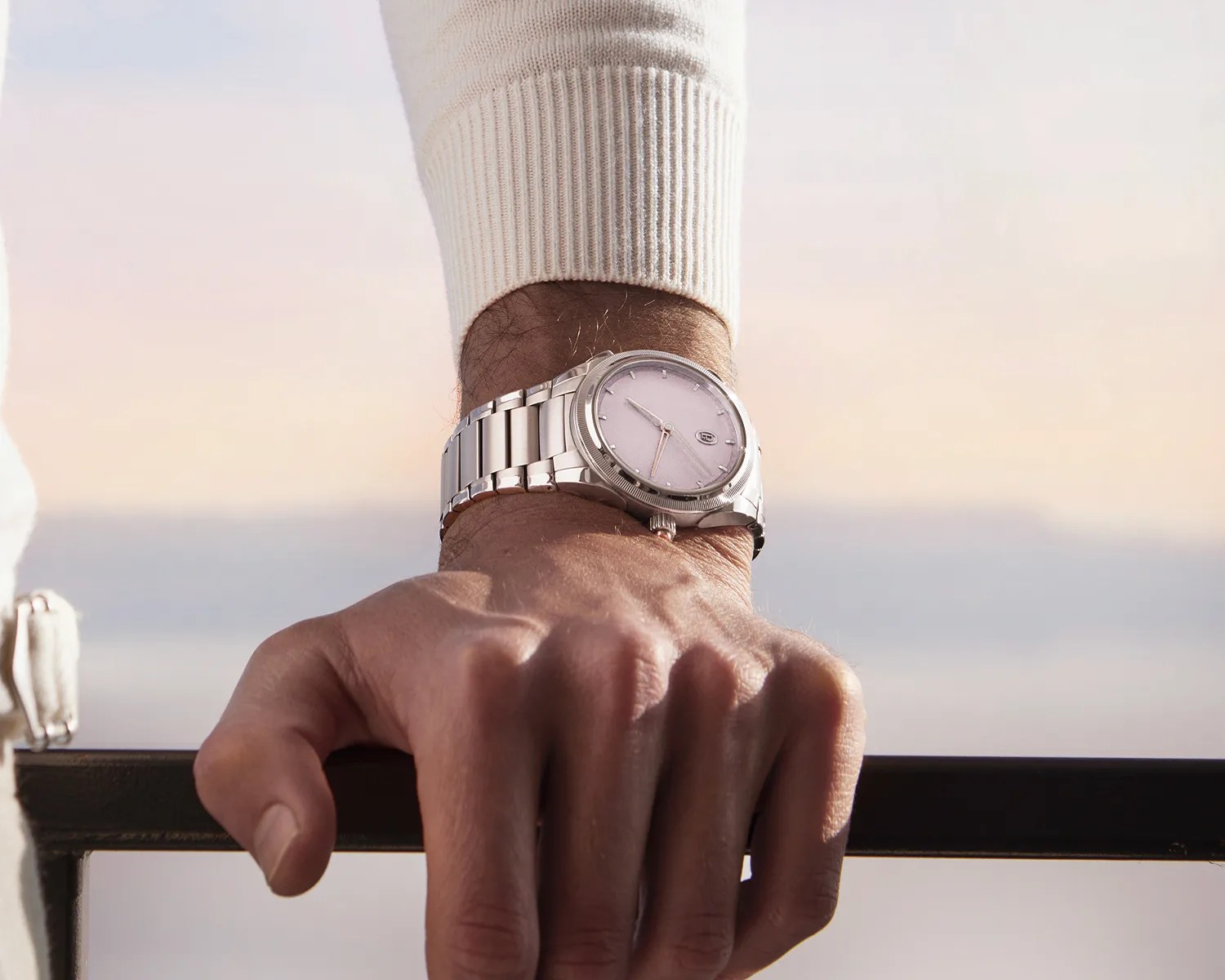 Silver metal wristwatch with a light-colored dial worn on a wrist over a white long-sleeve sweater.