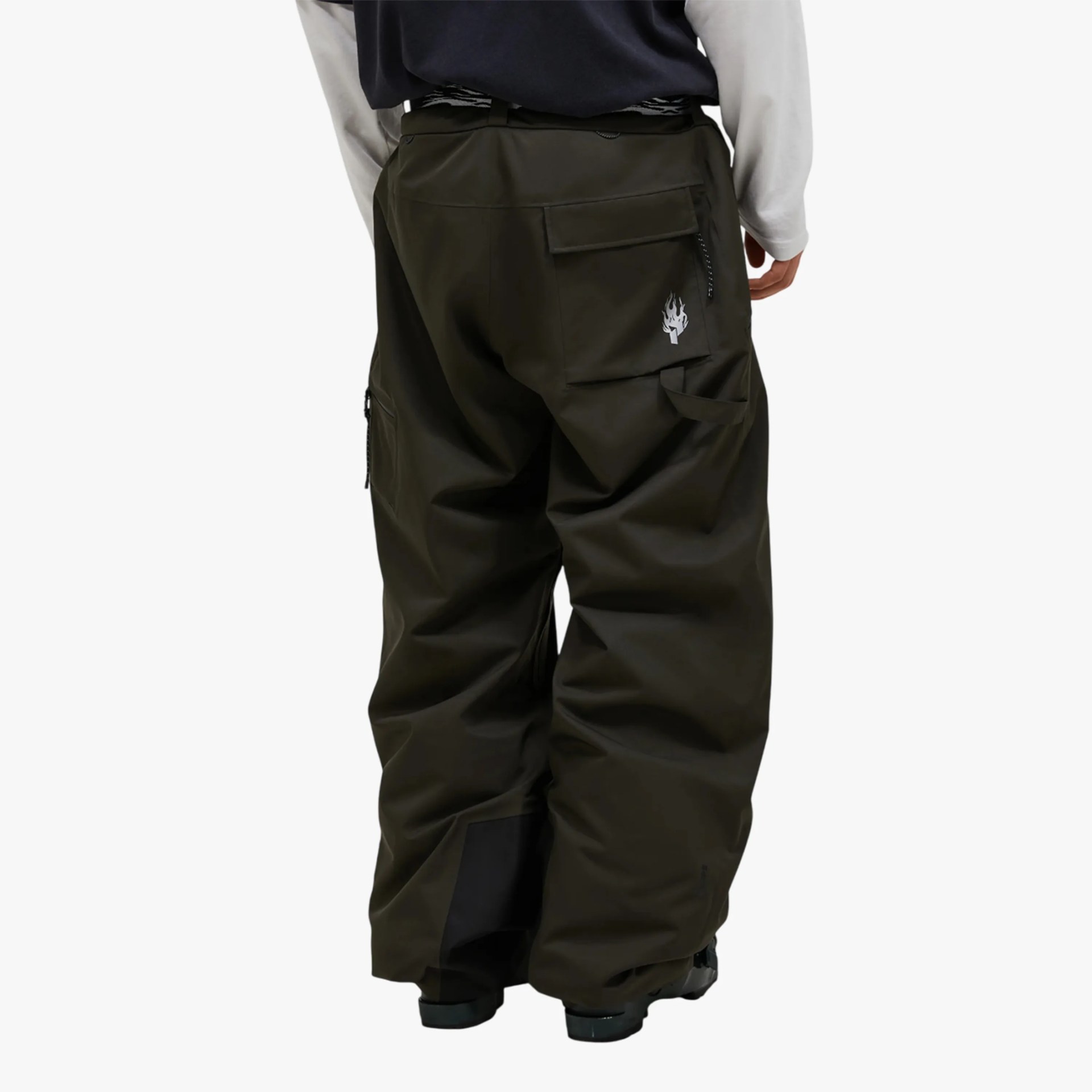 Loose dark olive green cargo pants with multiple pockets and a flame logo on the back pocket, worn by a person.