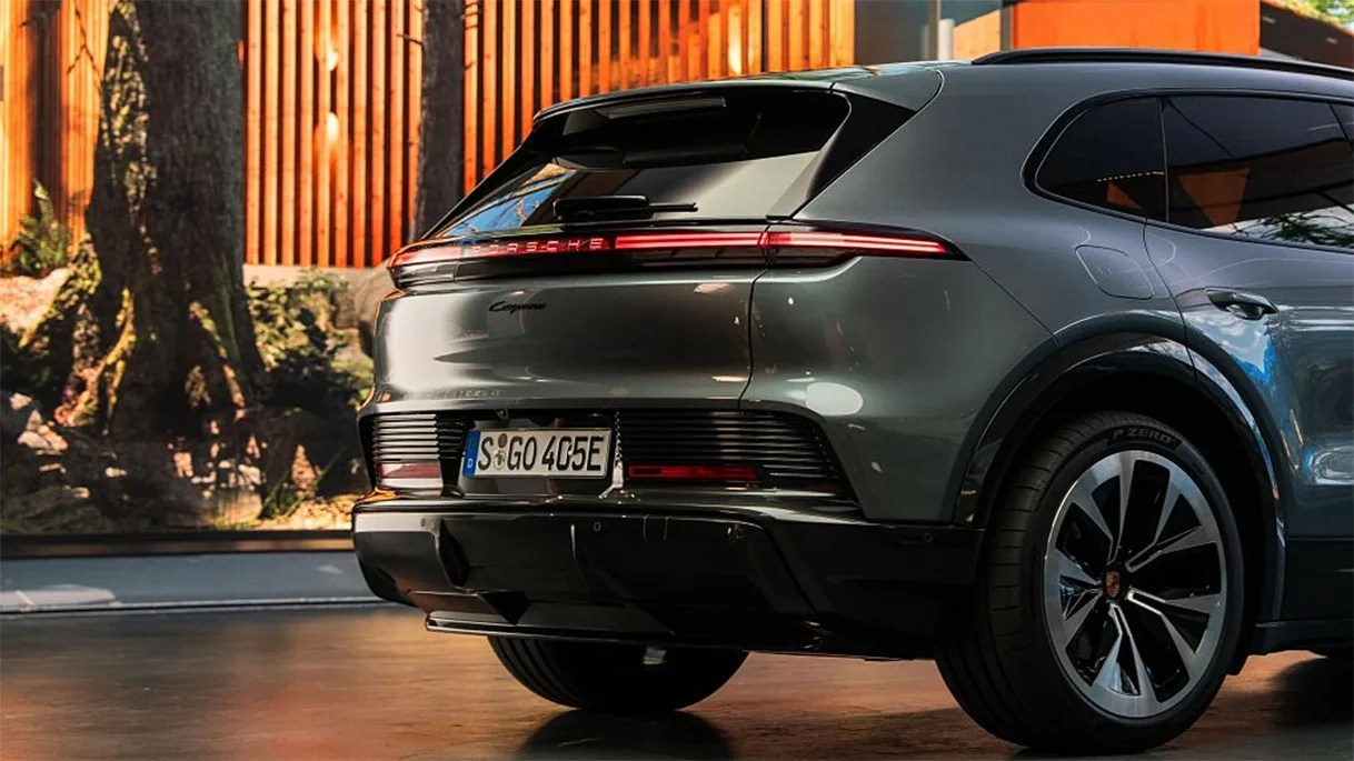 Rear view of a gray Porsche Cayenne SUV with illuminated rear light bar parked indoors near wooden paneling.