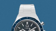 Silver metal wristwatch with a dark blue tachymeter bezel and black dial featuring three subdials and silver markers.