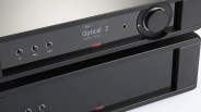 Black audio amplifier with digital display showing "Optical 2" input and control buttons on the front panel.