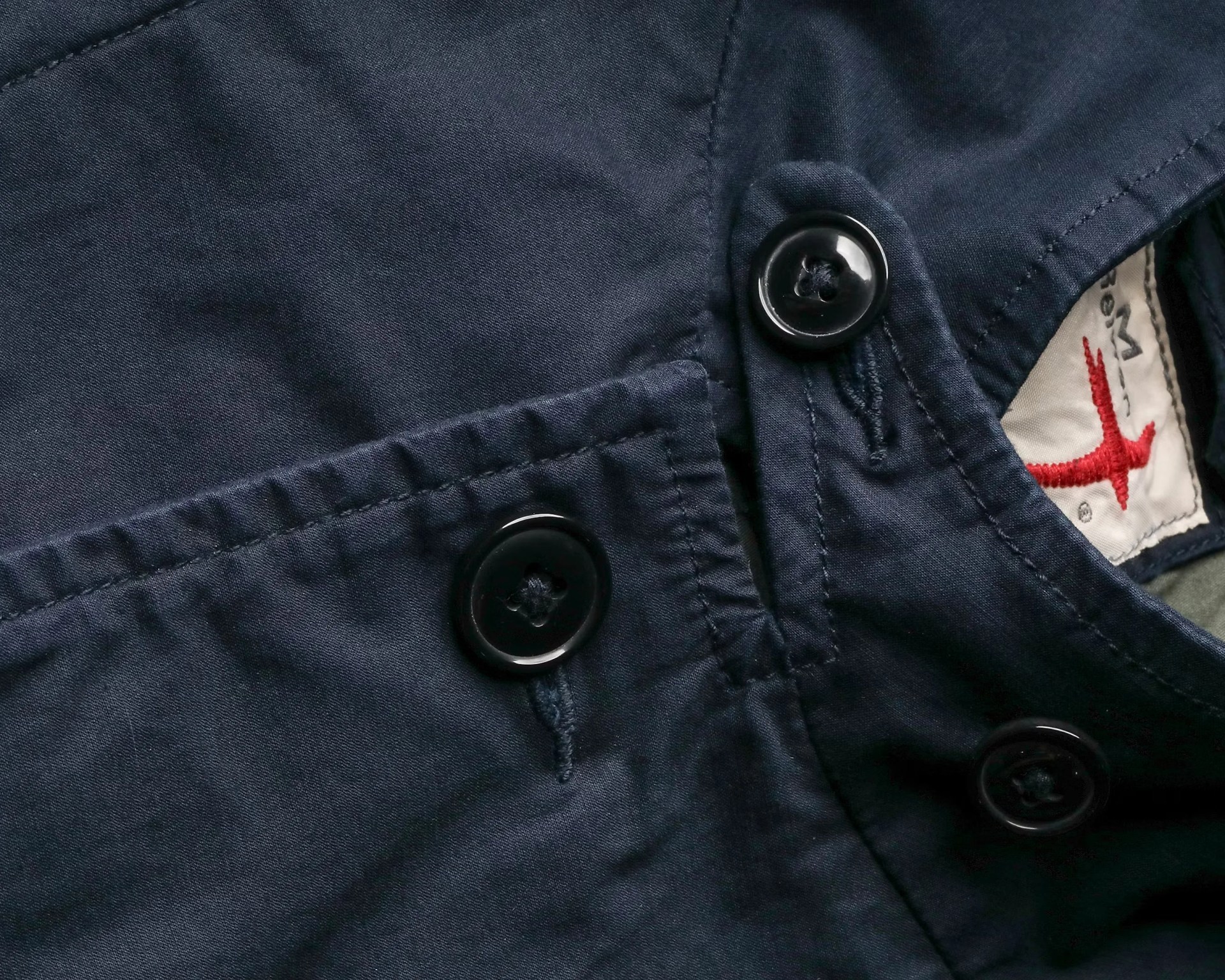 Close-up of a navy blue garment with black buttons and a partially visible white label with red embroidery.