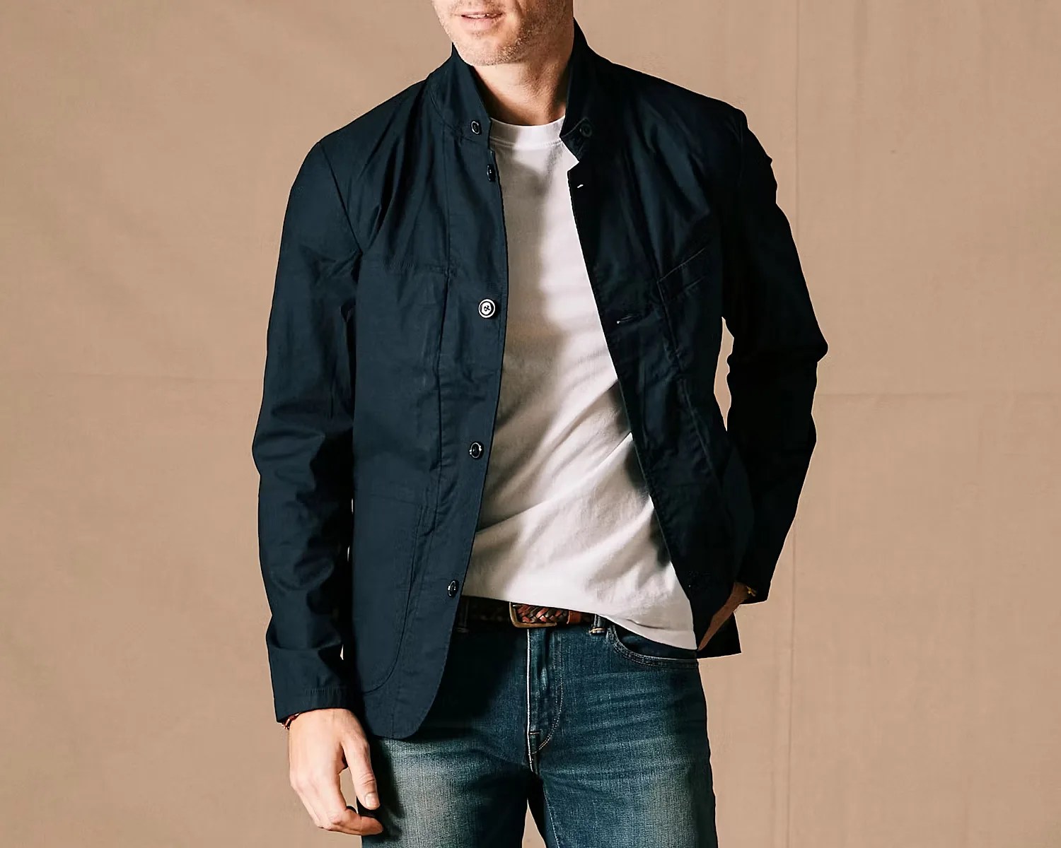 Man wearing a navy button-up jacket over a white t-shirt and blue jeans.