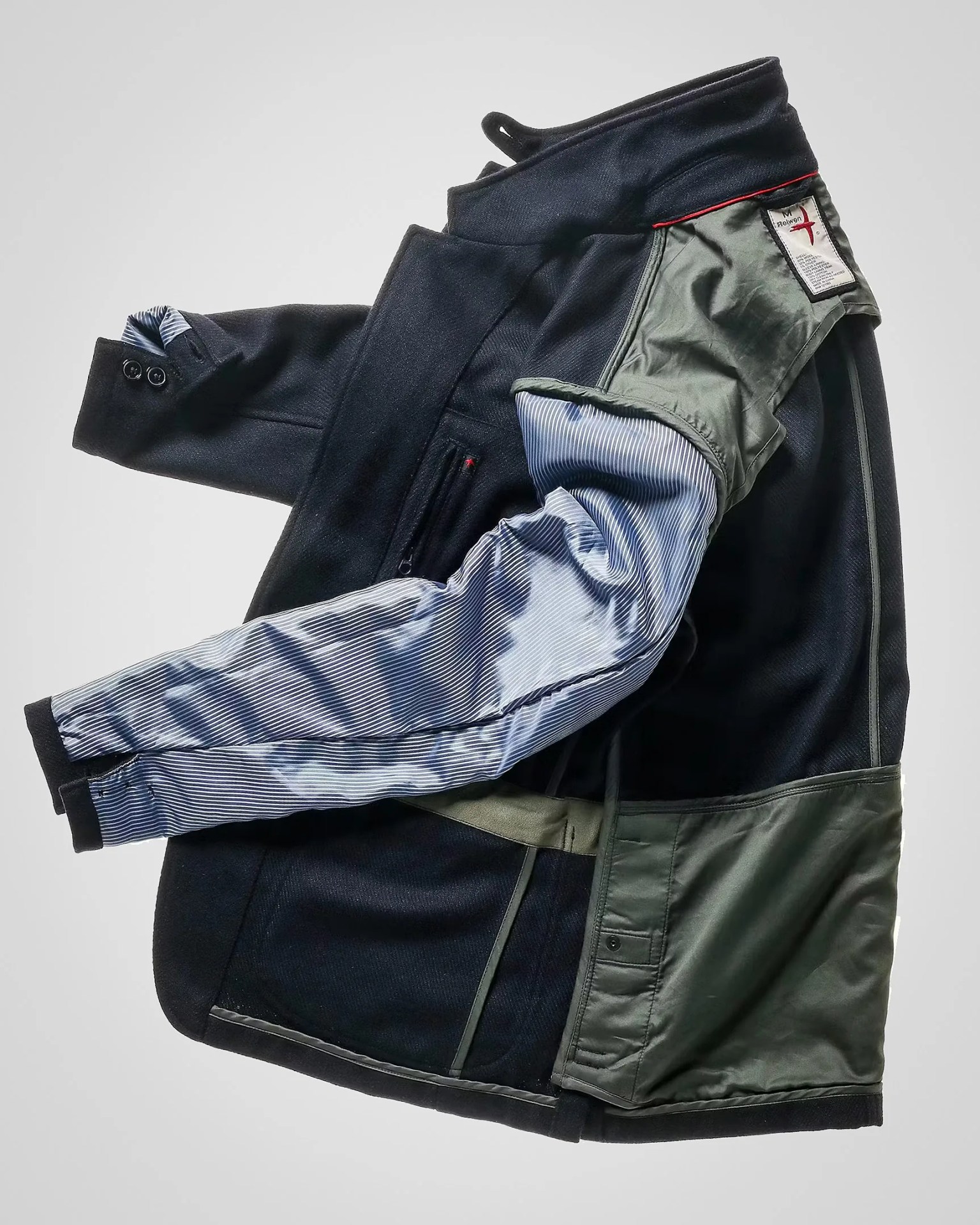 Black and olive green jacket with striped blue and white inner lining laid flat with one sleeve extended.