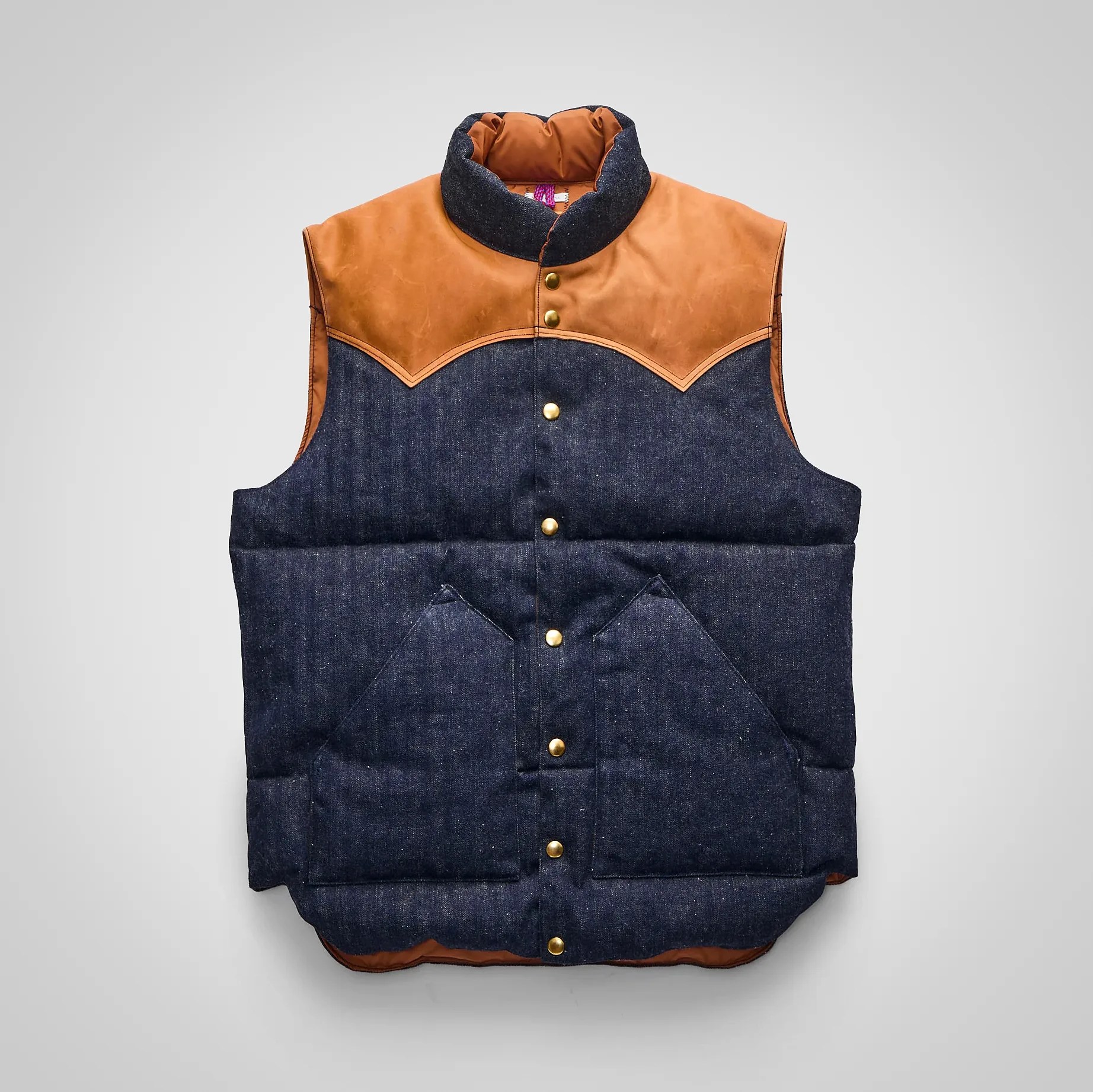 Padded sleeveless vest with dark denim body and brown leather yoke and collar, featuring gold snap buttons.
